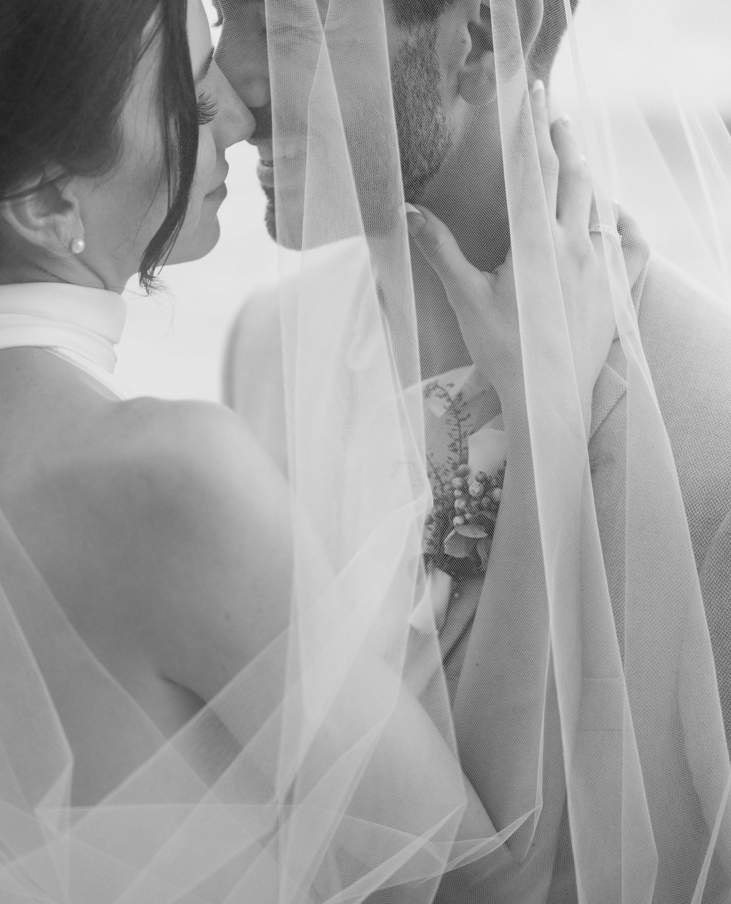 An intimate black and white portrait of a couple through delicate wedding veil.