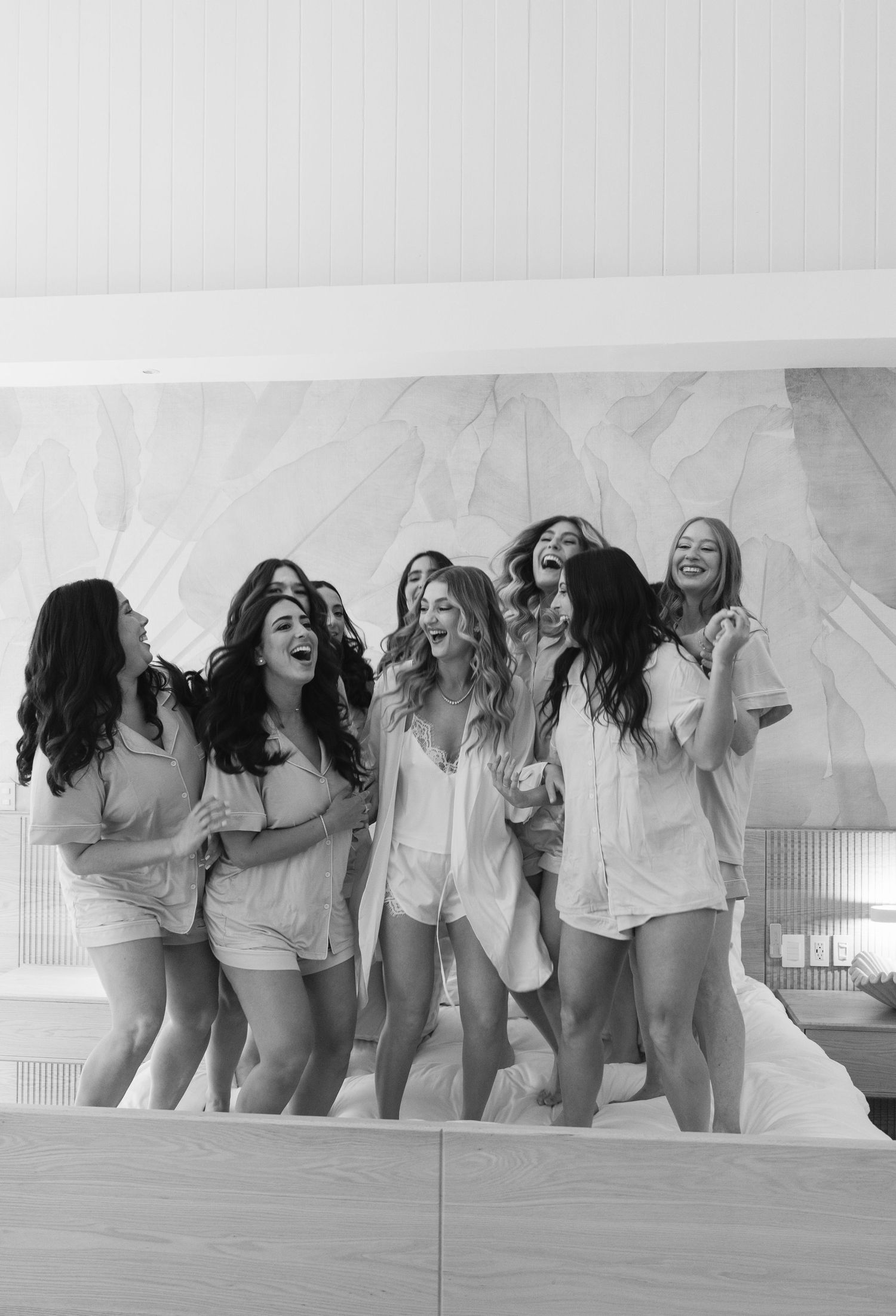 A group of people in white tops laugh and pose together in a black and white photo series.