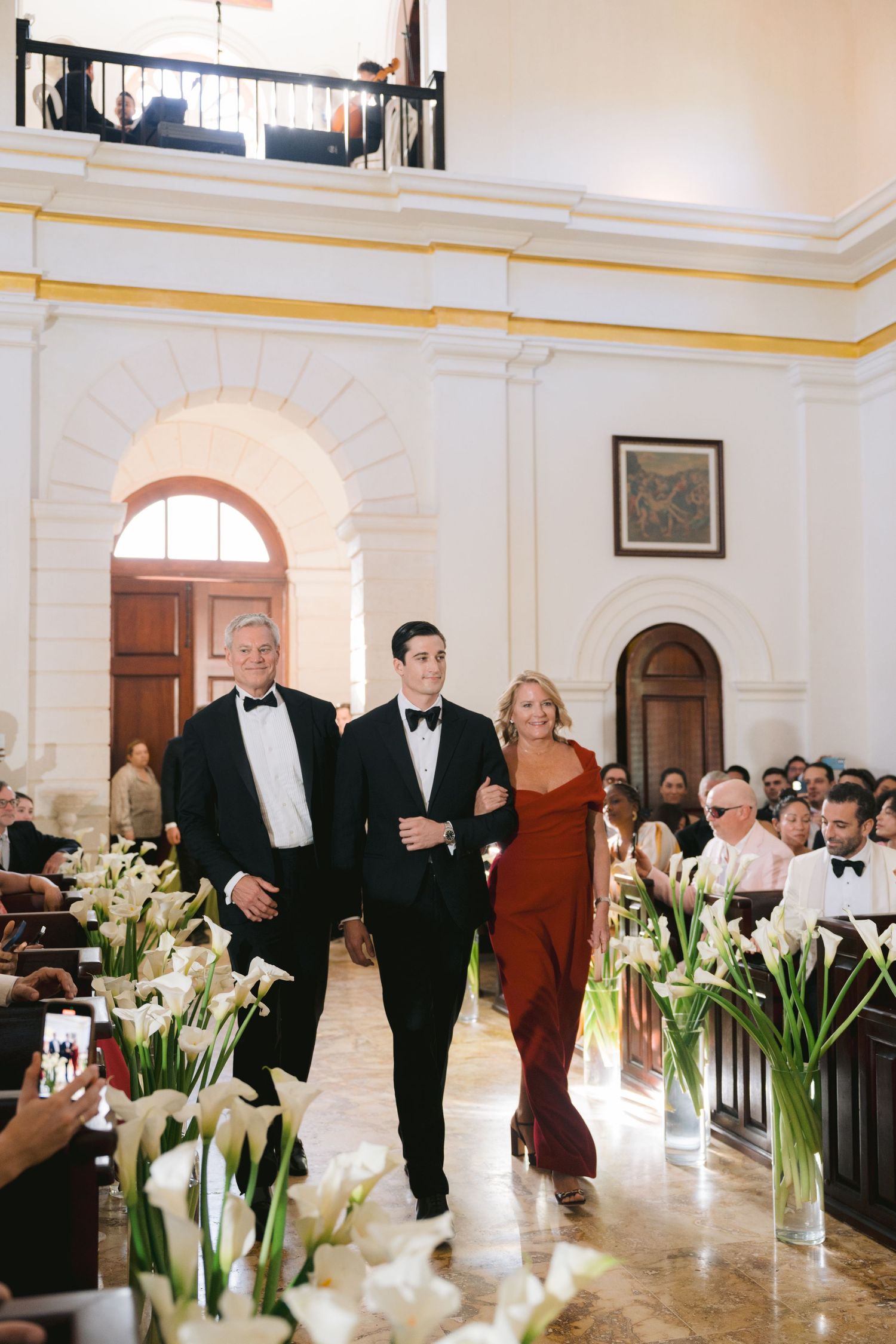Wedding processional down an elegant marble aisle lined with white calla lilies and guests in formal attire.