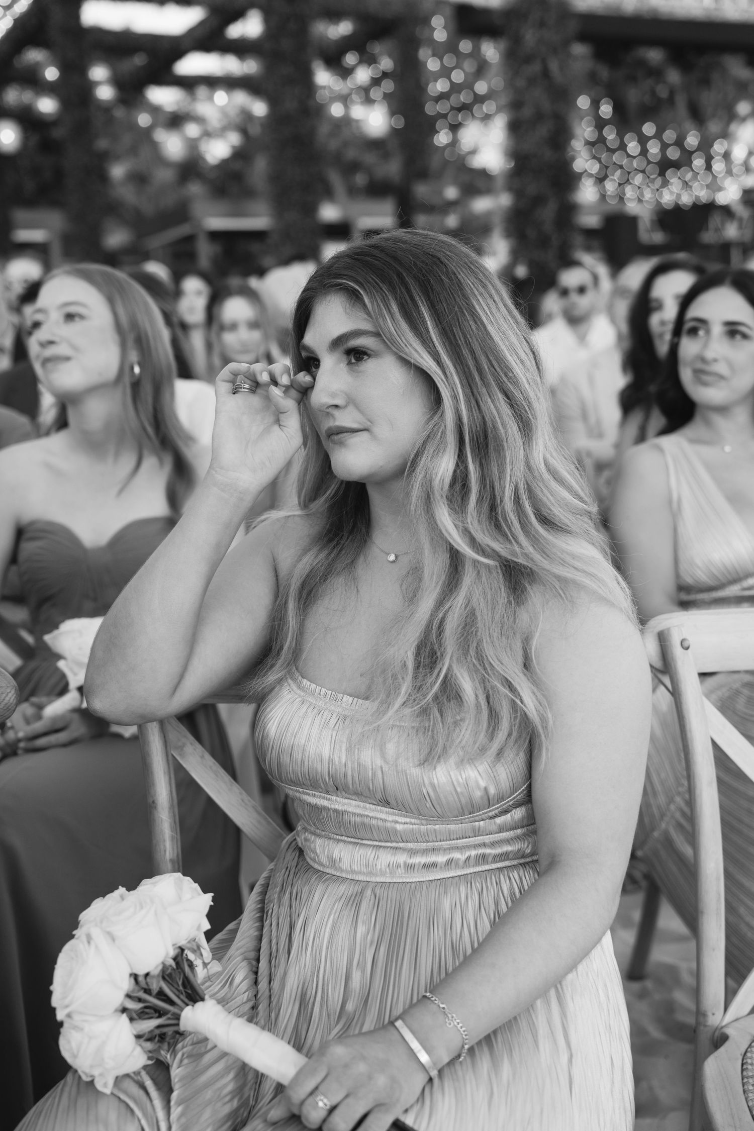 Wedding guests in champagne-colored dresses sit together at an outdoor celebration.