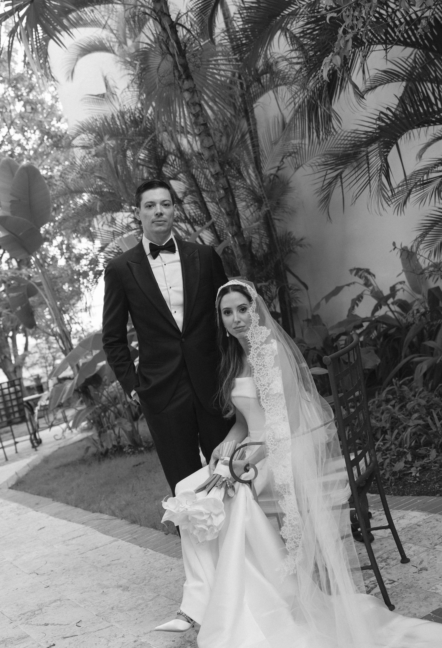 A black and white wedding portrait of a couple posing among tropical palm trees.