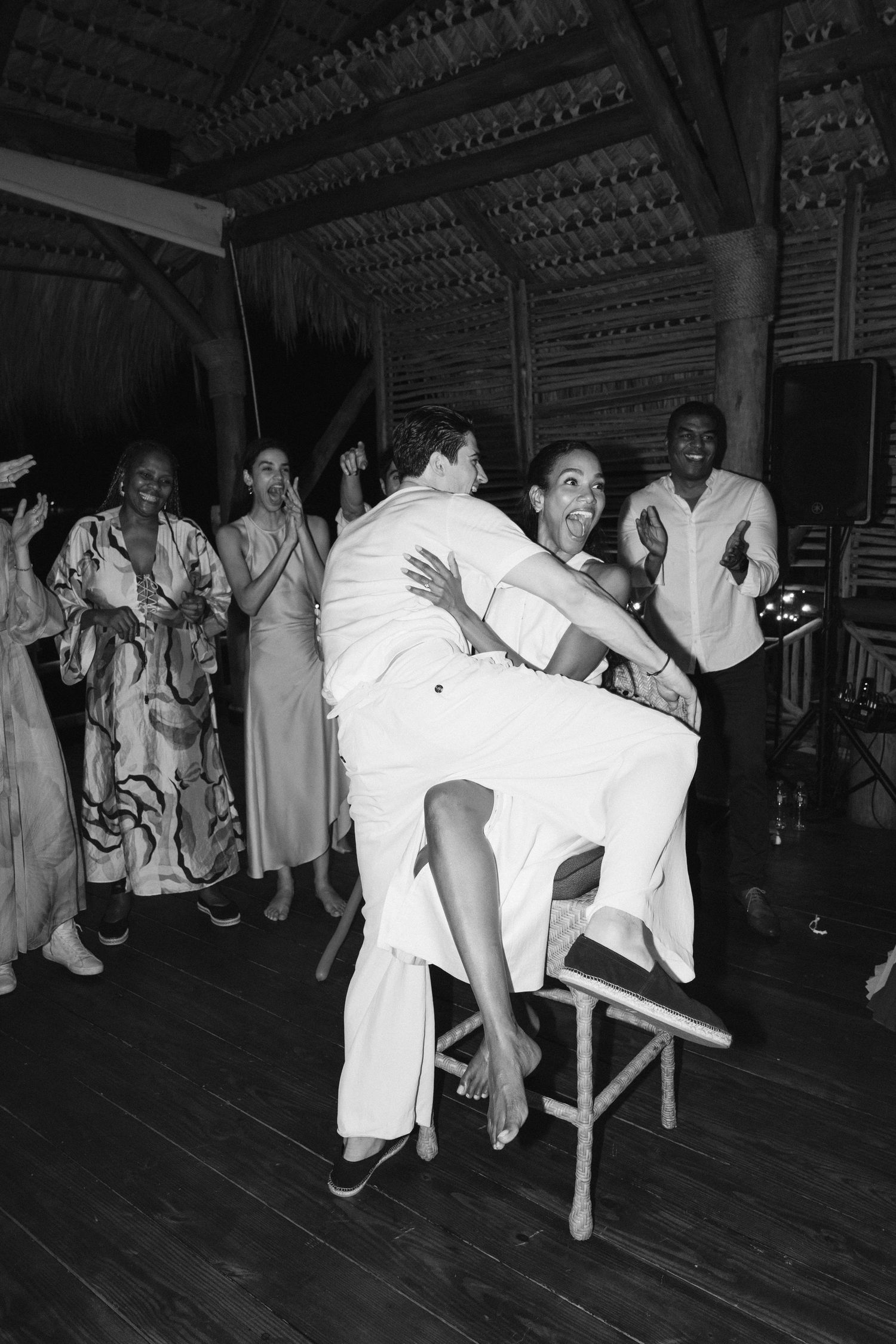 People in white lab coats race around a dimly lit wooden dance floor during an energetic relay competition.