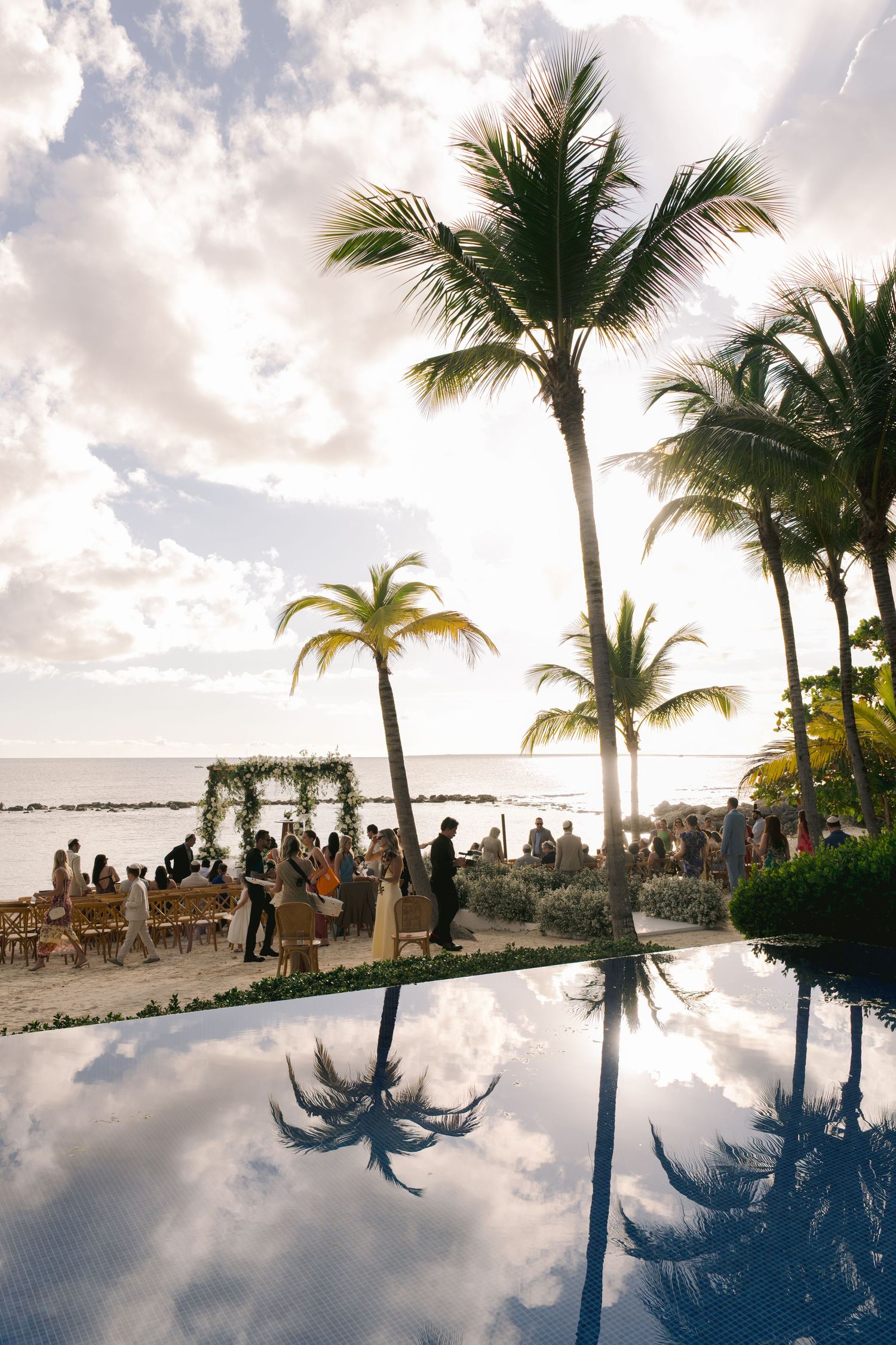 A beachfront wedding ceremony setup with palm trees and infinity pool reflection during golden hour in Hawaii.