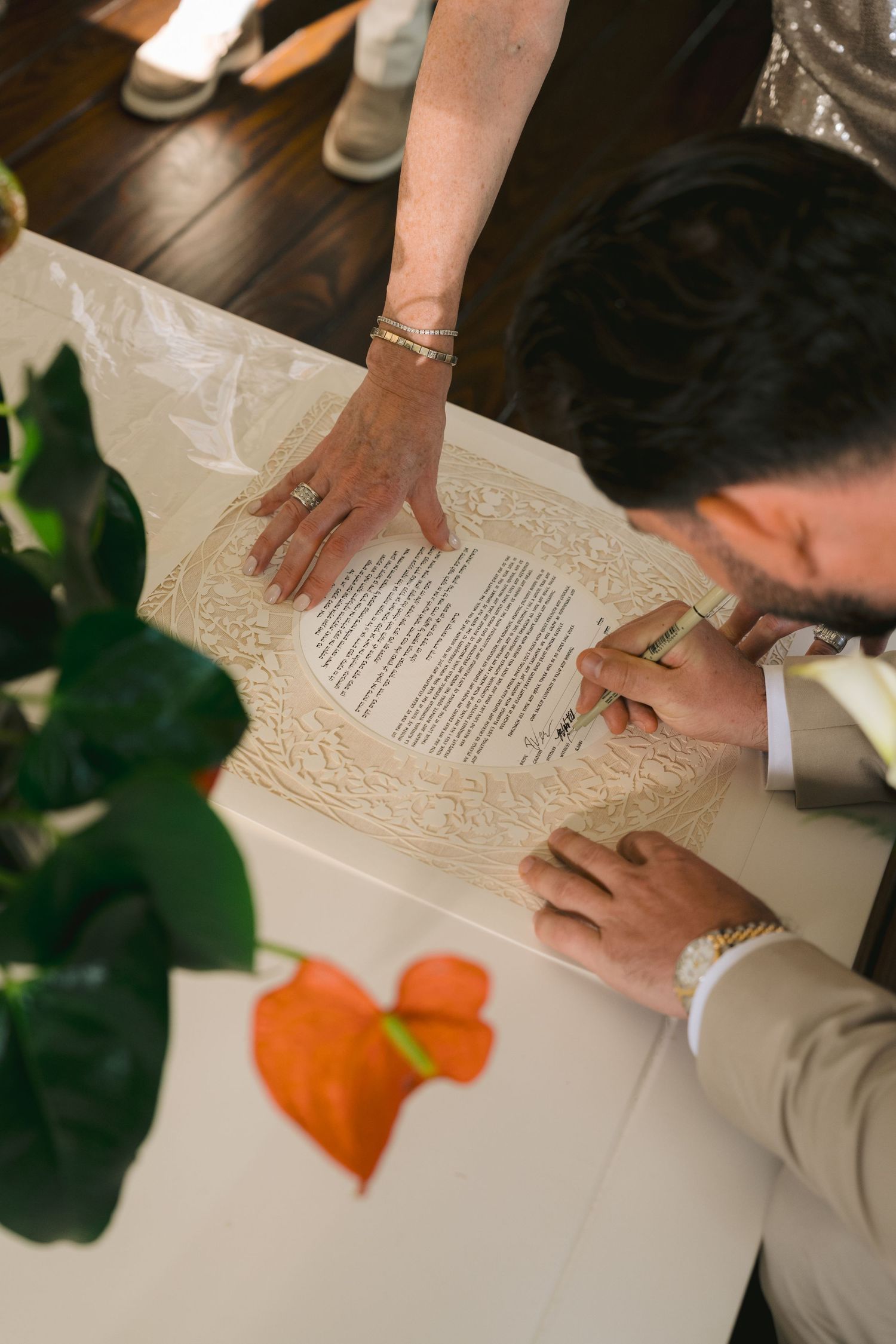 Close-up view of hands signing important documents on a white table with orange and green decorative elements.
