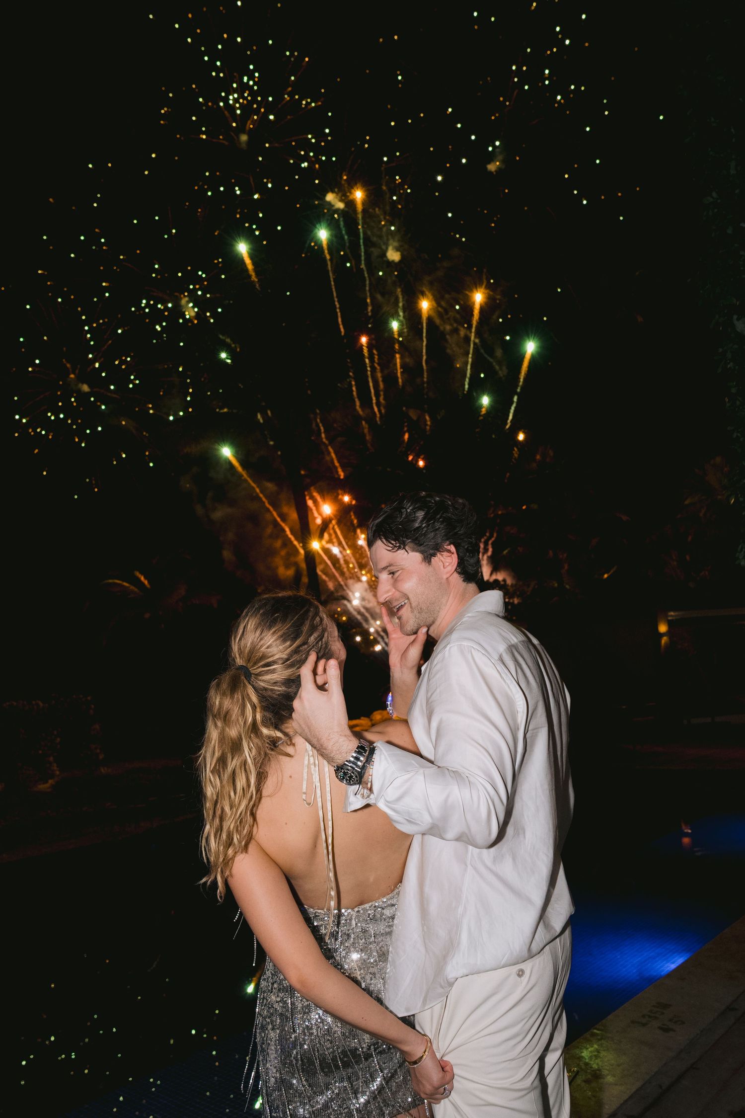 A couple dances together at night under sparkling fireworks and glowing lights in a romantic celebration.