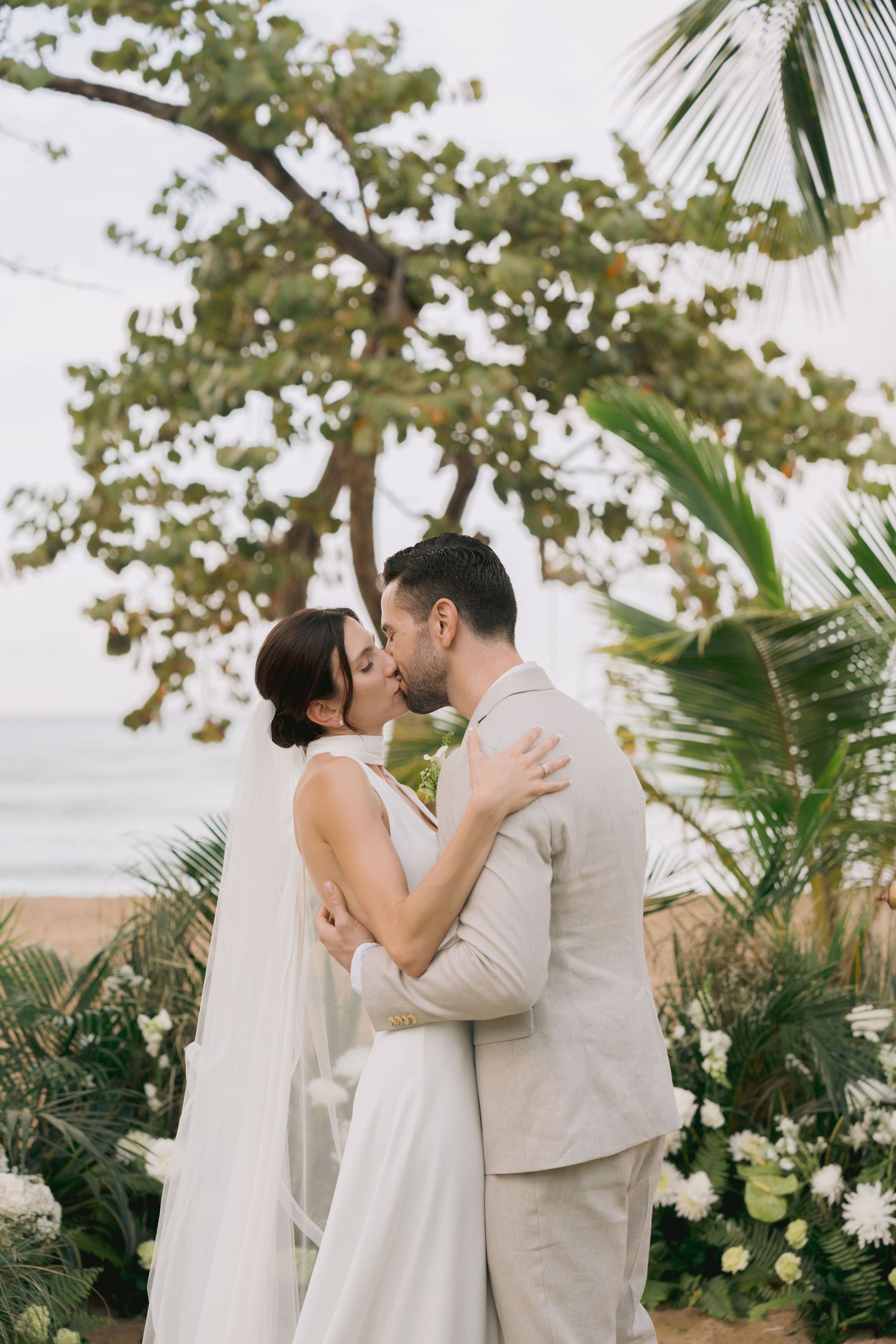 A romantic moment between newlyweds surrounded by palm trees and tropical foliage.