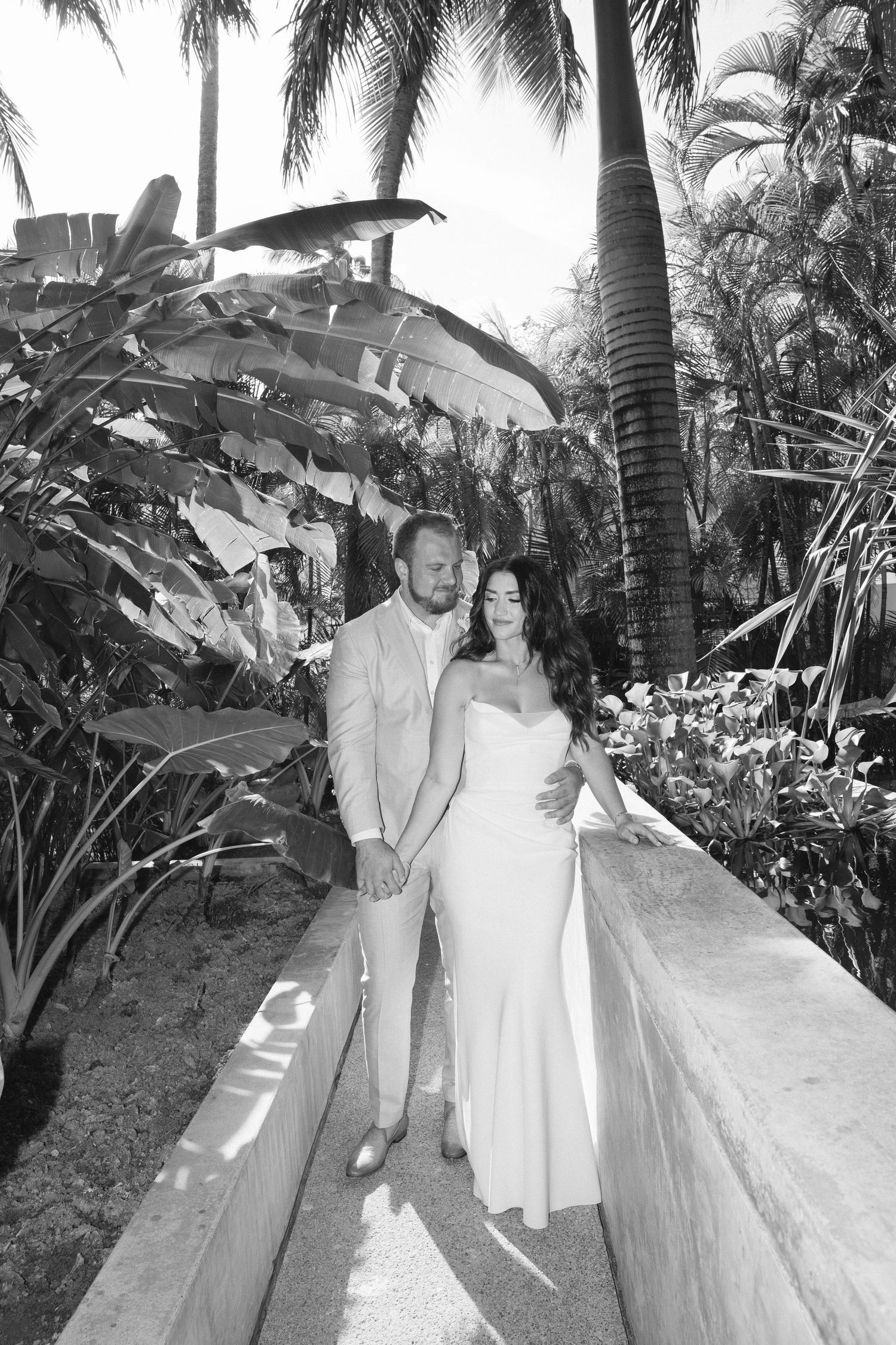 Black and white tropical wedding photo with palm trees and lush garden pathway.