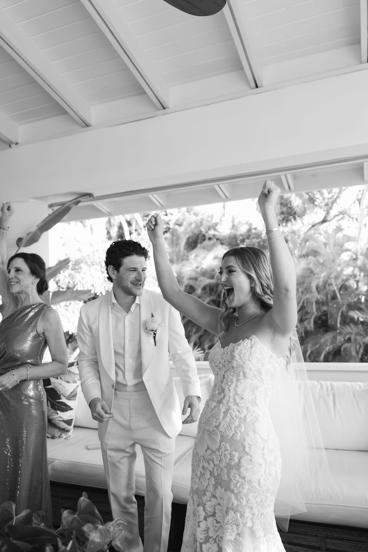 Wedding party celebrates with joyful dancing and raised arms under a white tent during reception.