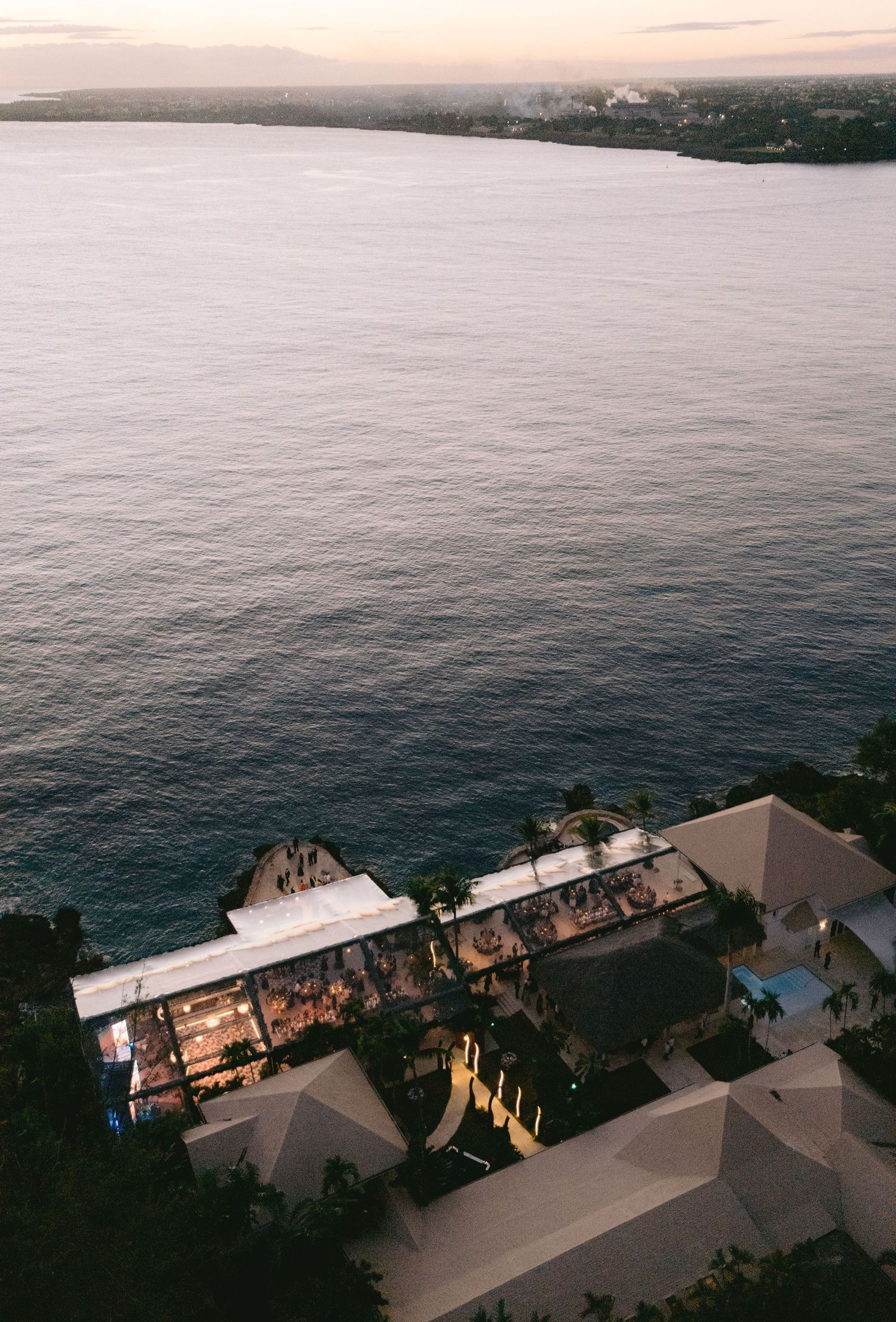 Aerial view of a coastal resort property with a pool overlooking the ocean at dusk.