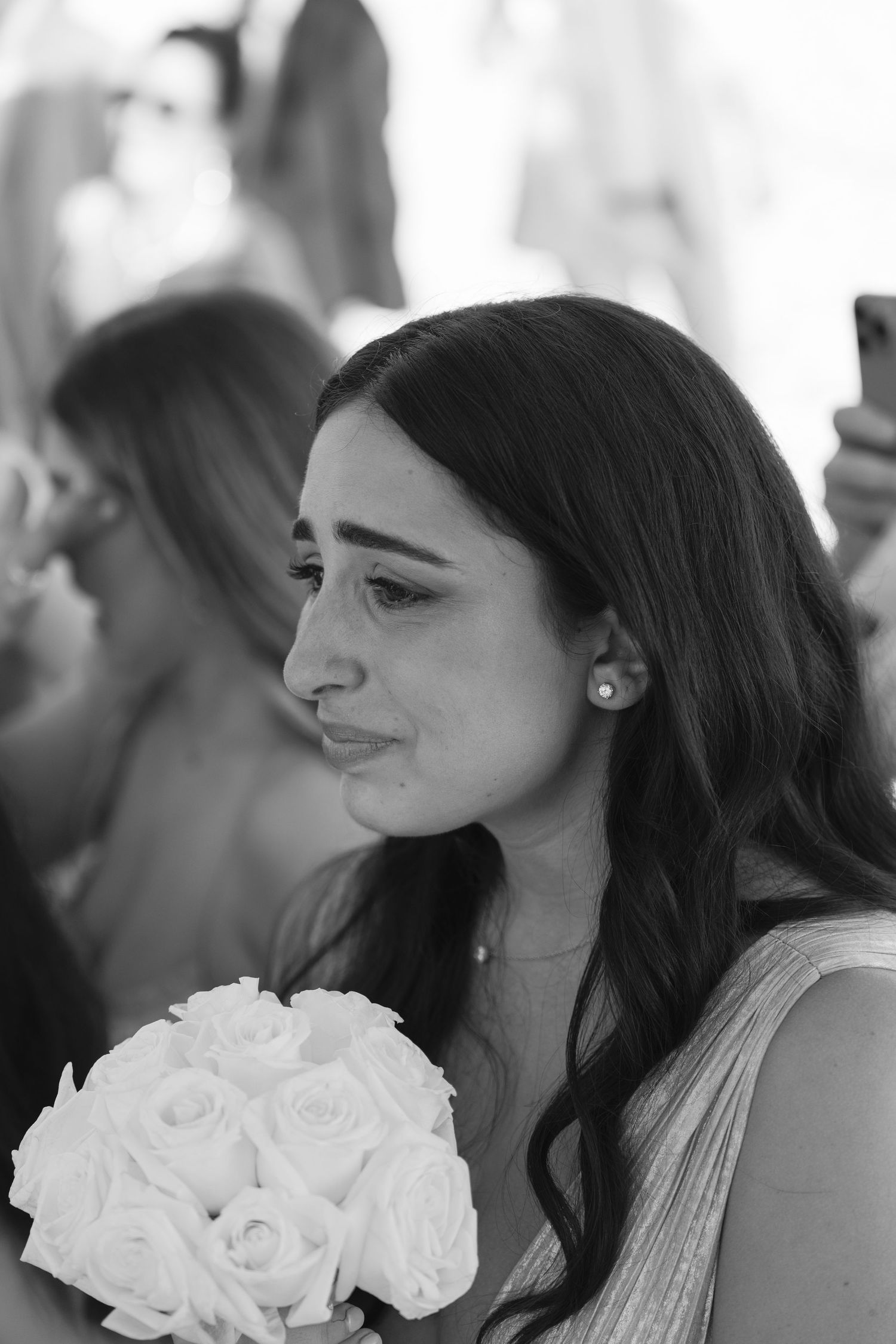 Black and white photo of an emotional bridesmaid holding a white rose bouquet at a wedding ceremony.