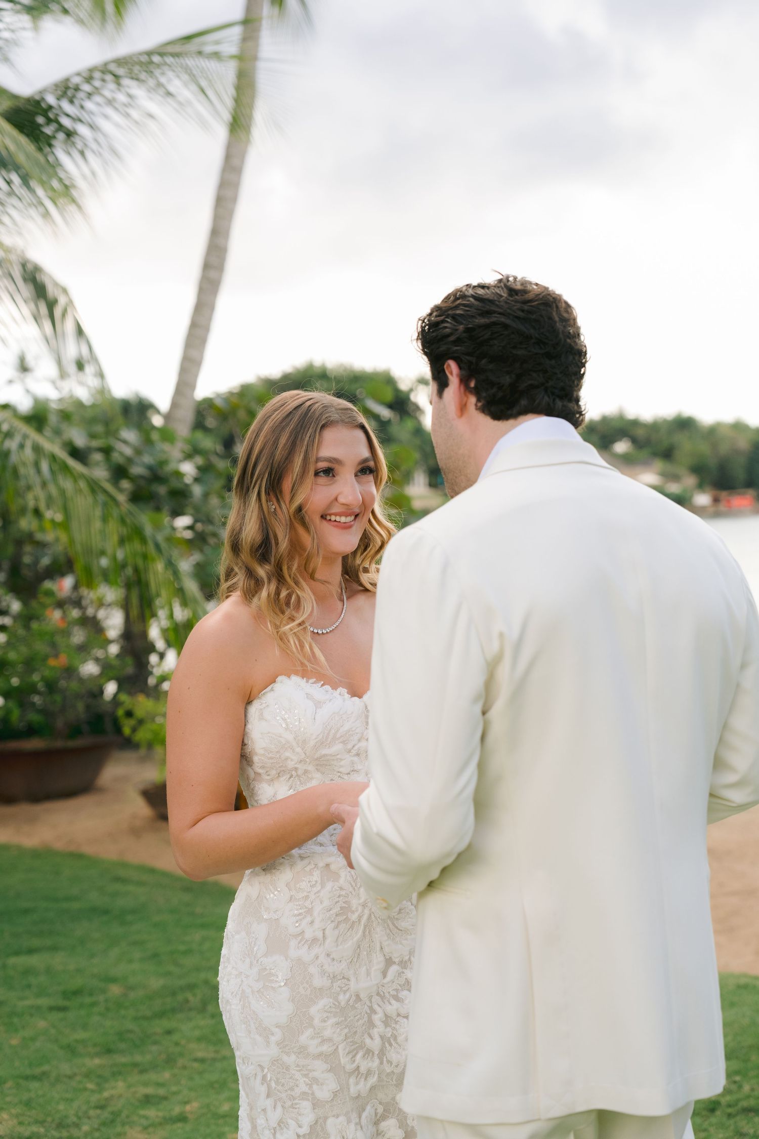A couple shares a romantic moment during their tropical wedding ceremony with palm trees in the background.