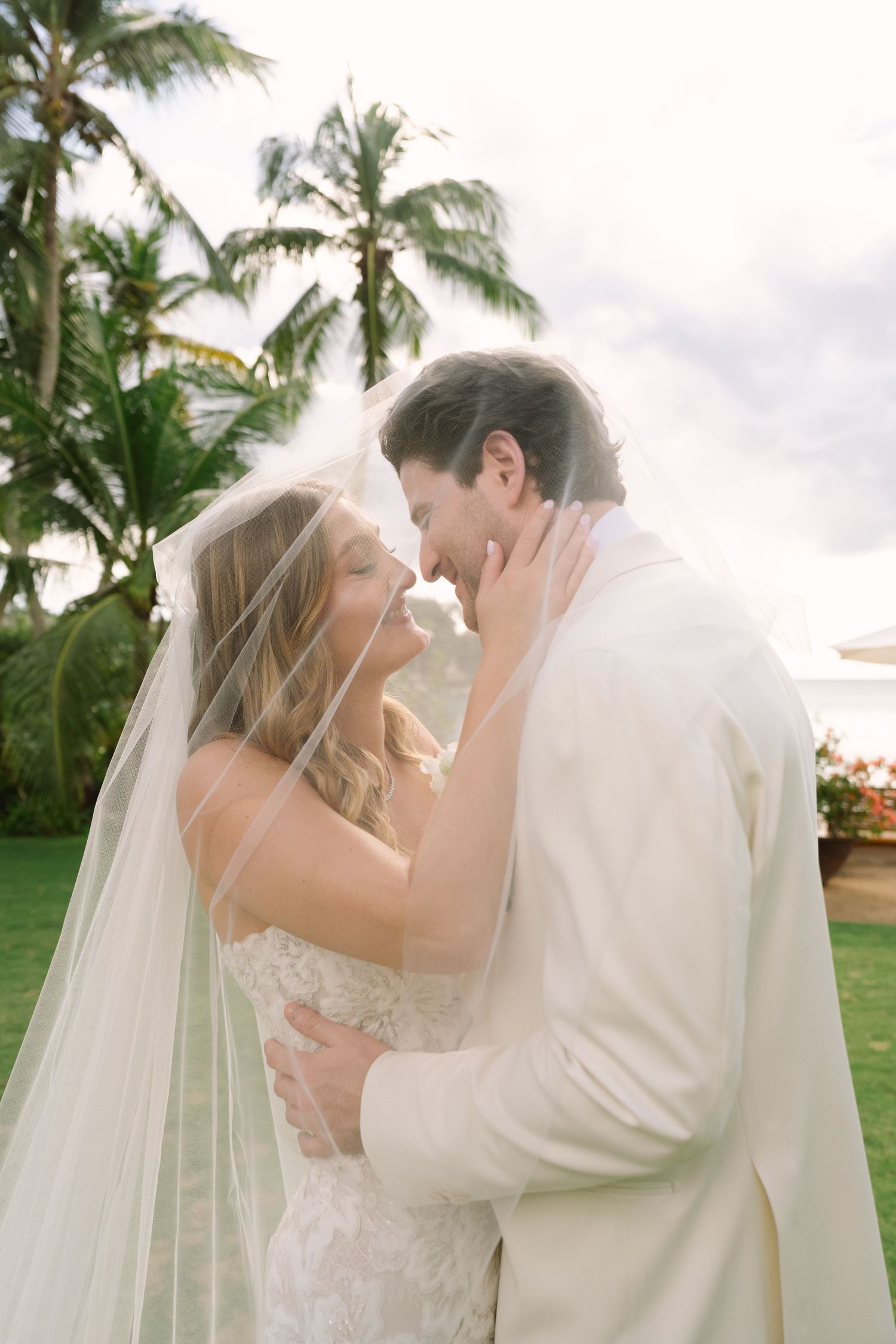 A romantic wedding moment captured between newlyweds embracing under palm trees at a tropical destination.
