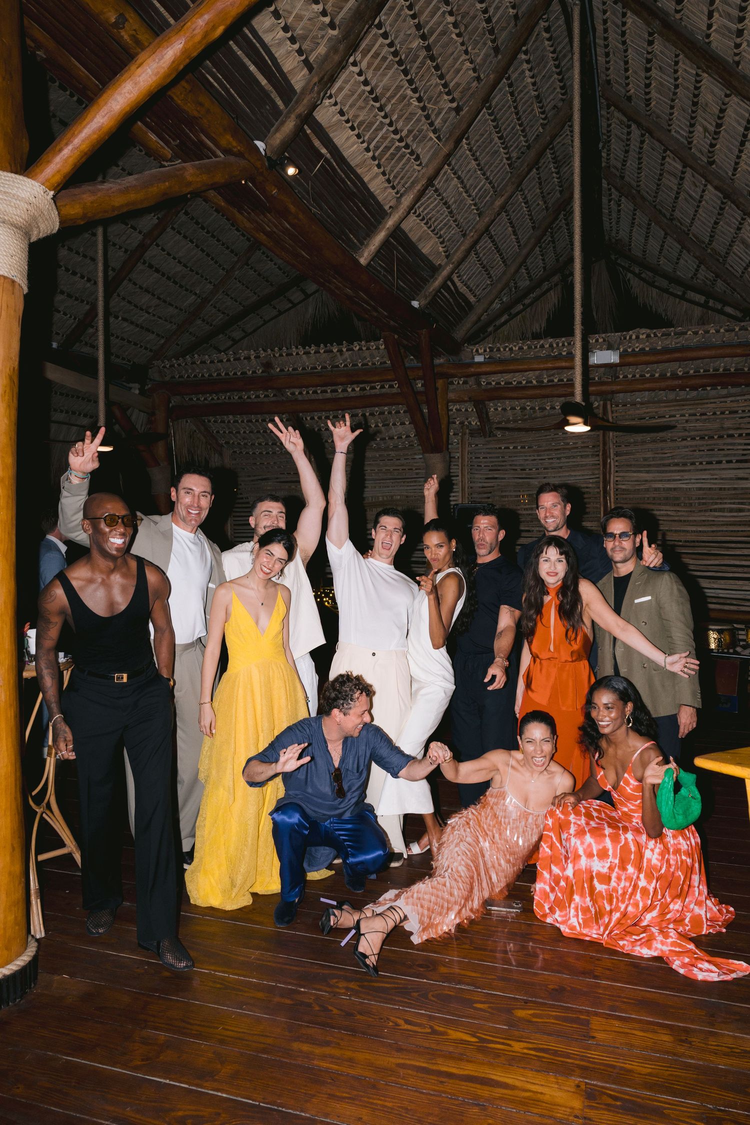 Group of people posing together in casual and formal attire inside a rustic venue with wooden floors and high ceilings.