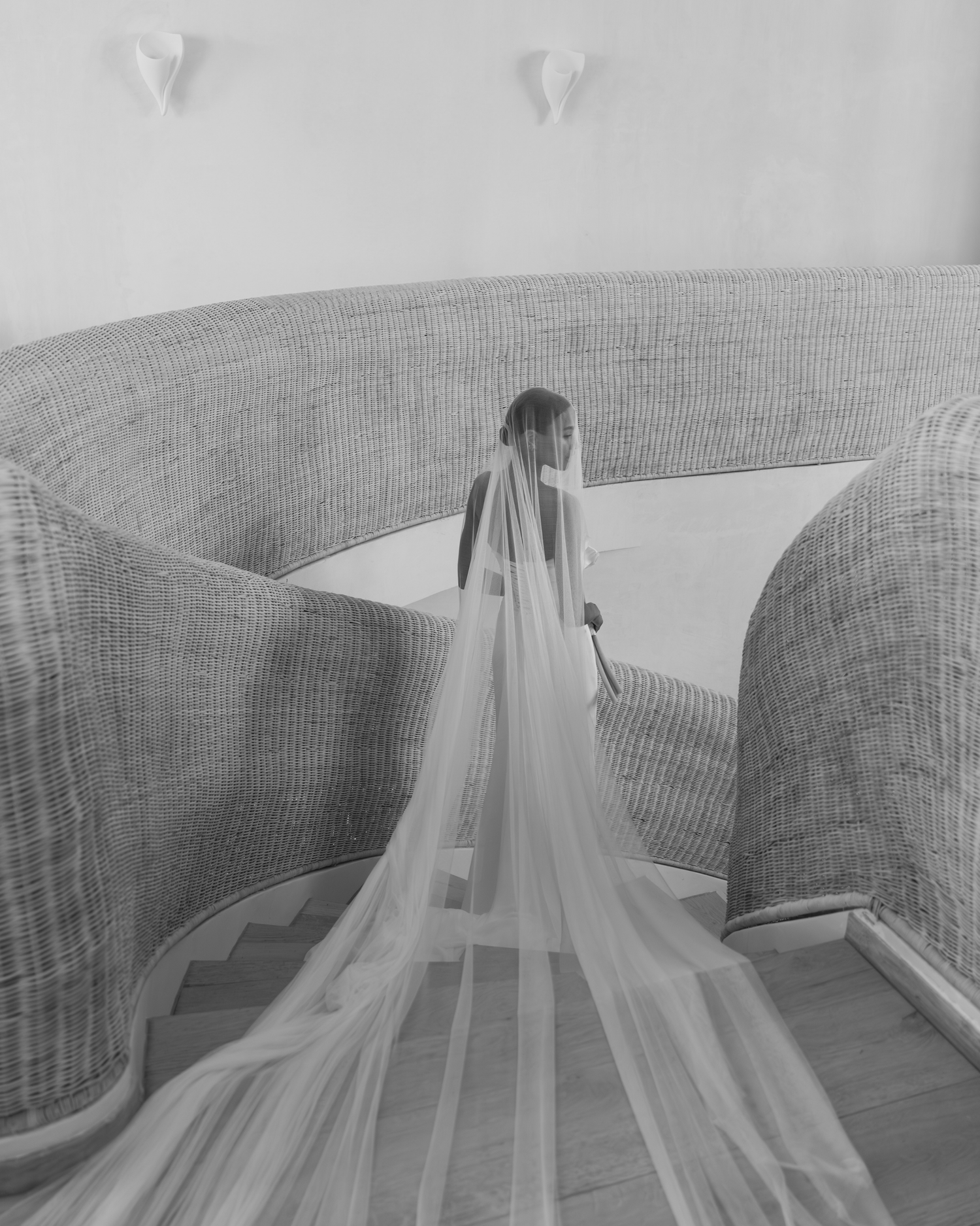 A bride in a flowing cathedral veil stands between curved walls, creating a dramatic black and white composition.