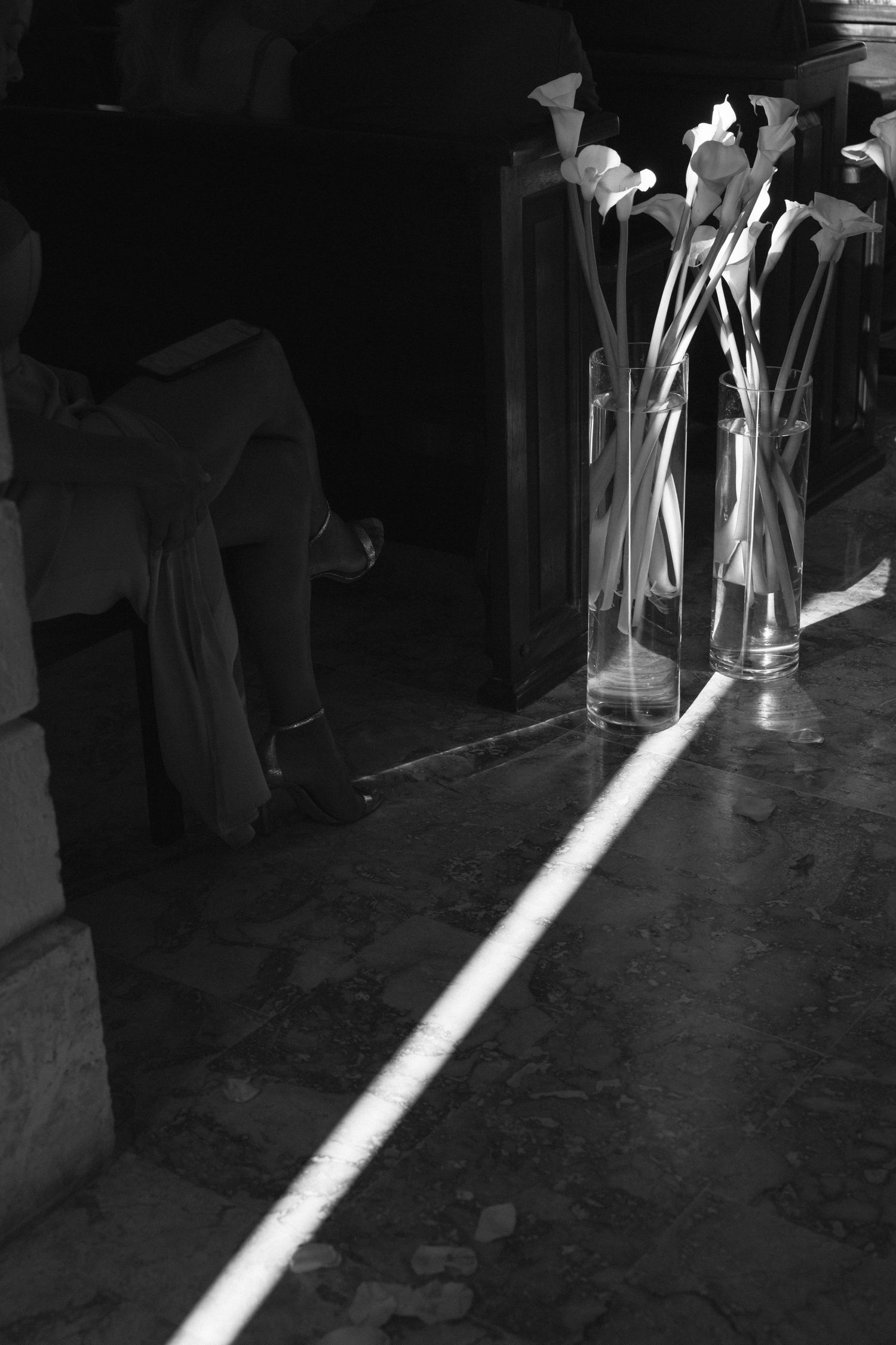 A dramatic black and white image of calla lilies in glass vases with stark lighting creating a striking ray of light.
