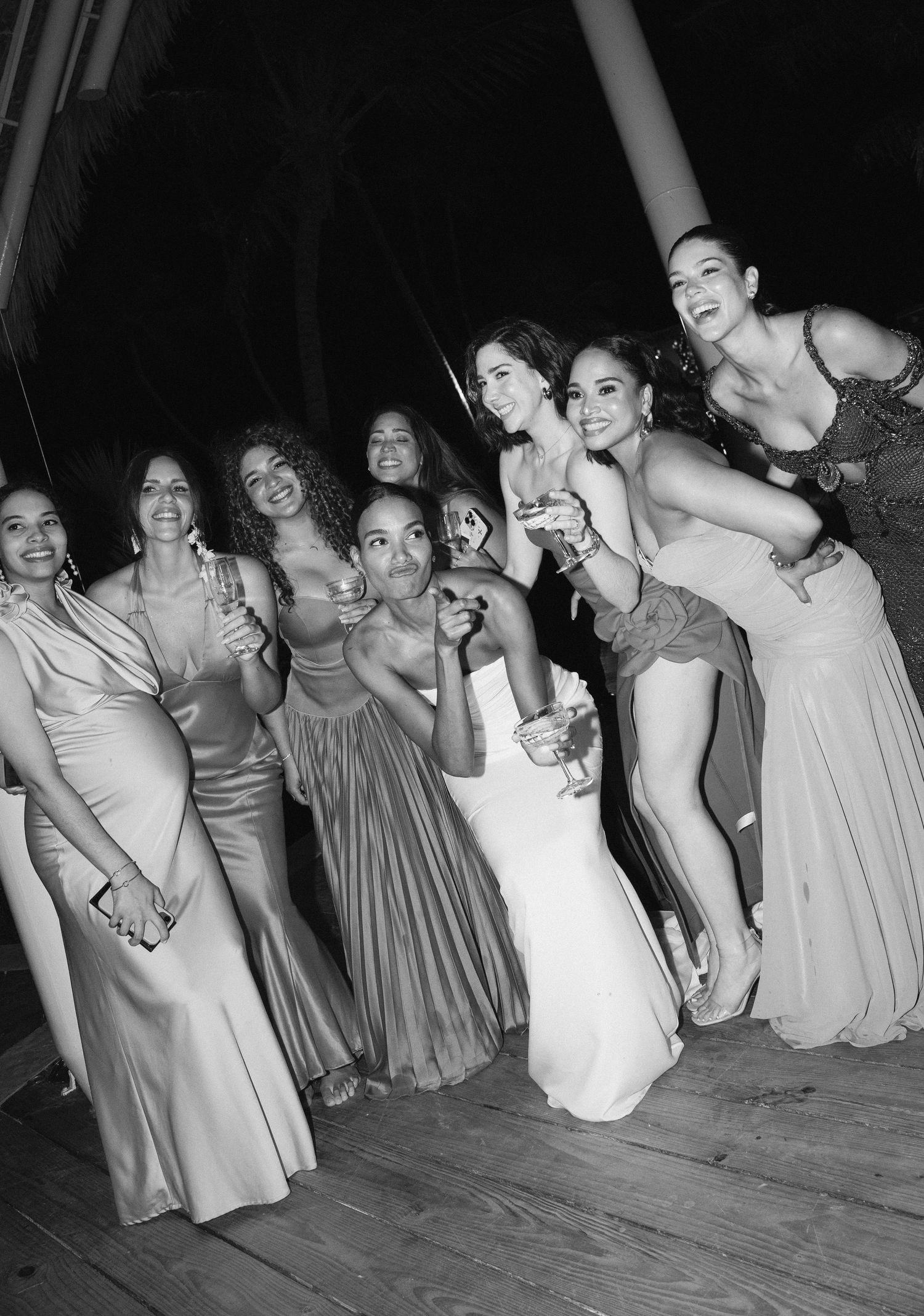 A group of bridesmaids and a bride pose together at a wedding celebration, laughing joyfully in black and white.