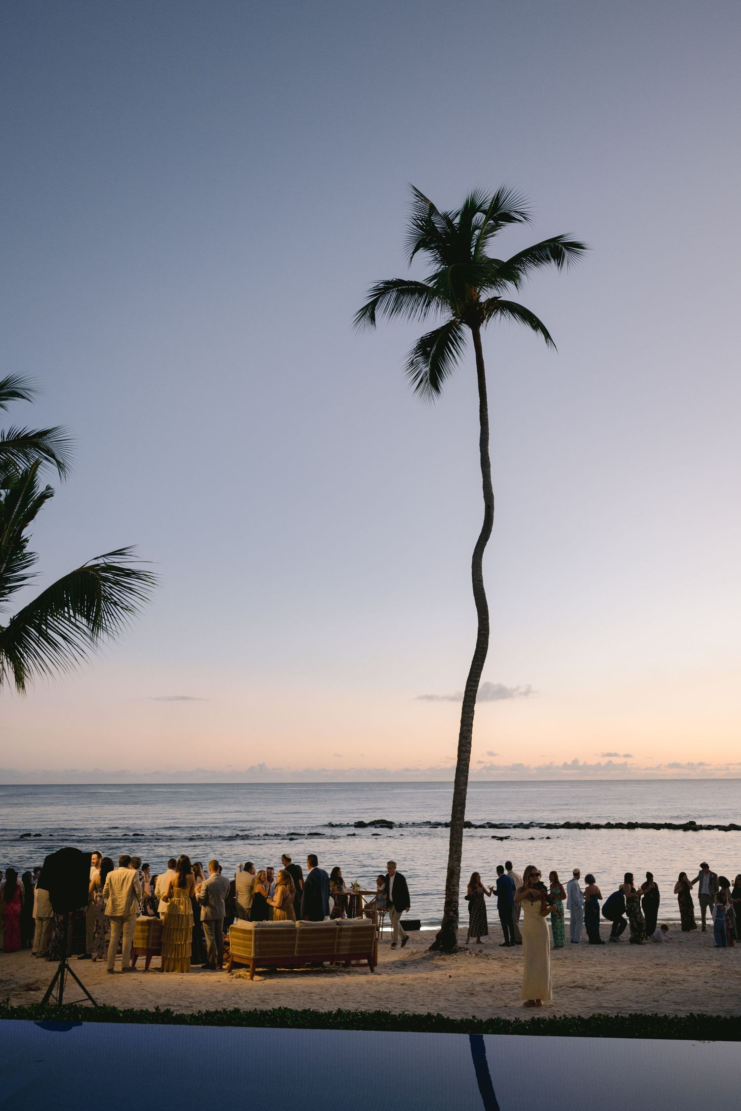 Silhouettes of people gathered on a beach at sunset with palm trees and ocean views in Hawaii.