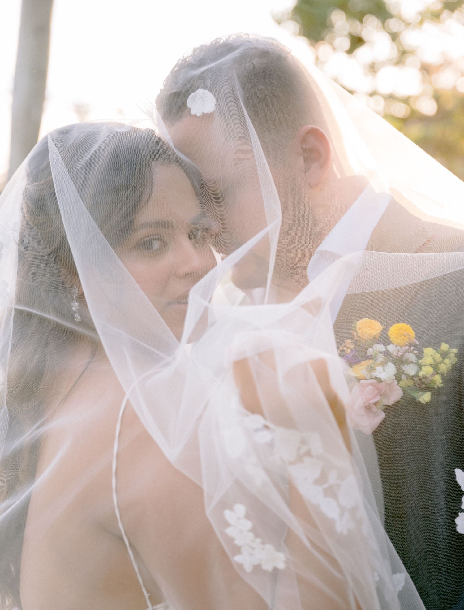 A romantic moment captured through delicate wedding veil during golden hour.