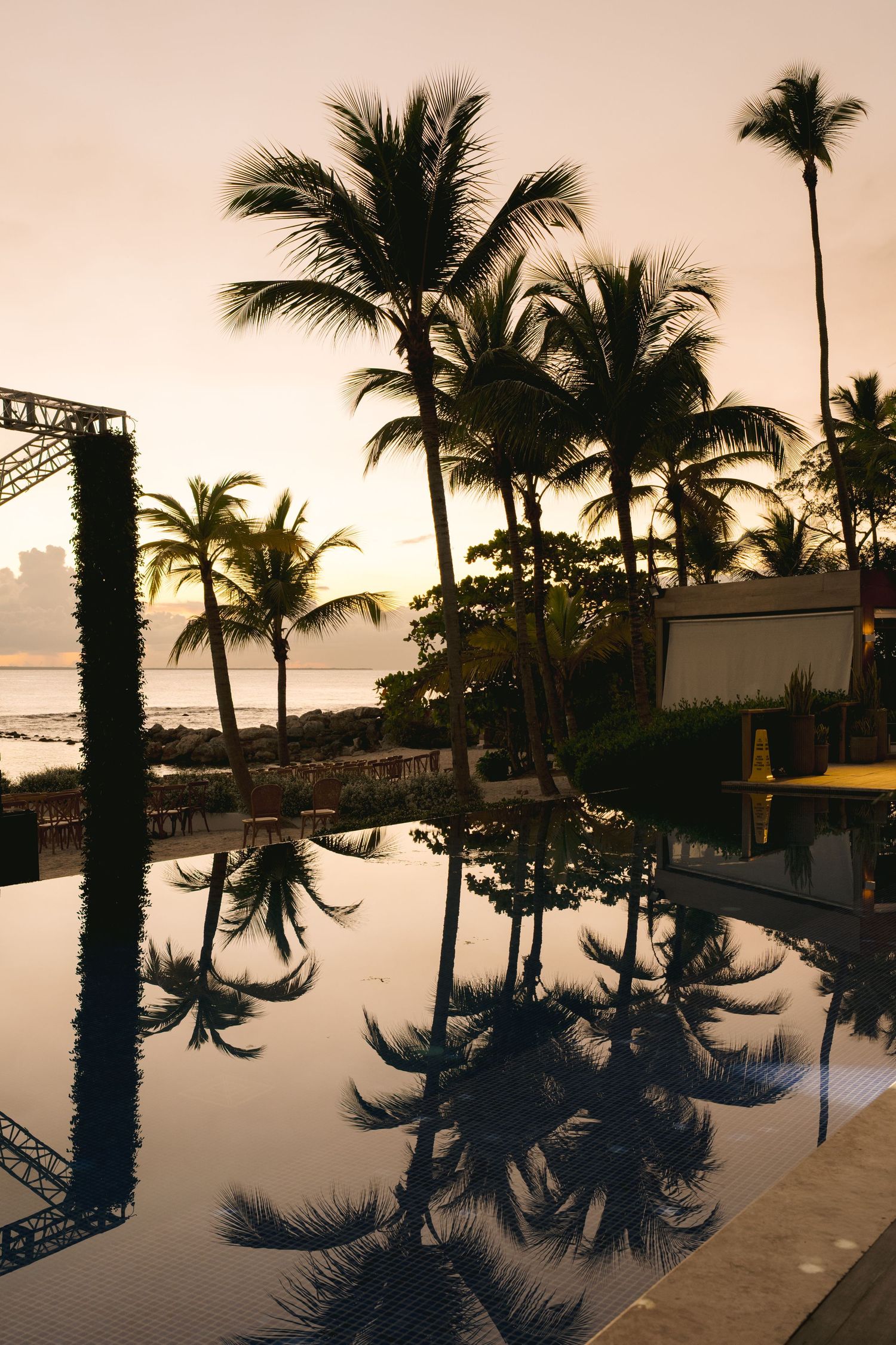 Palm trees reflect in an infinity pool at sunset with ocean views at a tropical resort in Hawaii.