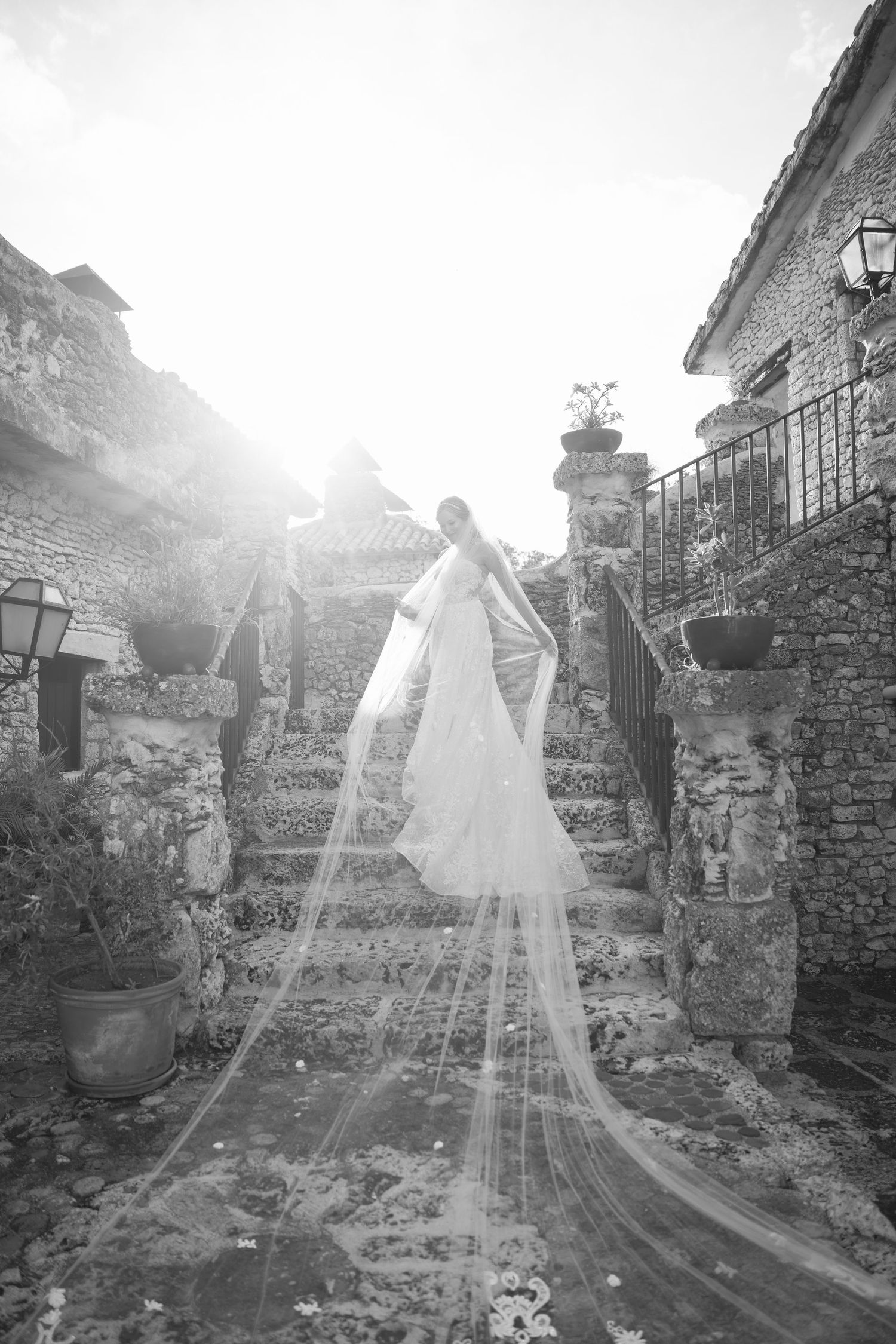 Long flowing bridal veil cascading down stone steps in romantic black and white photography.