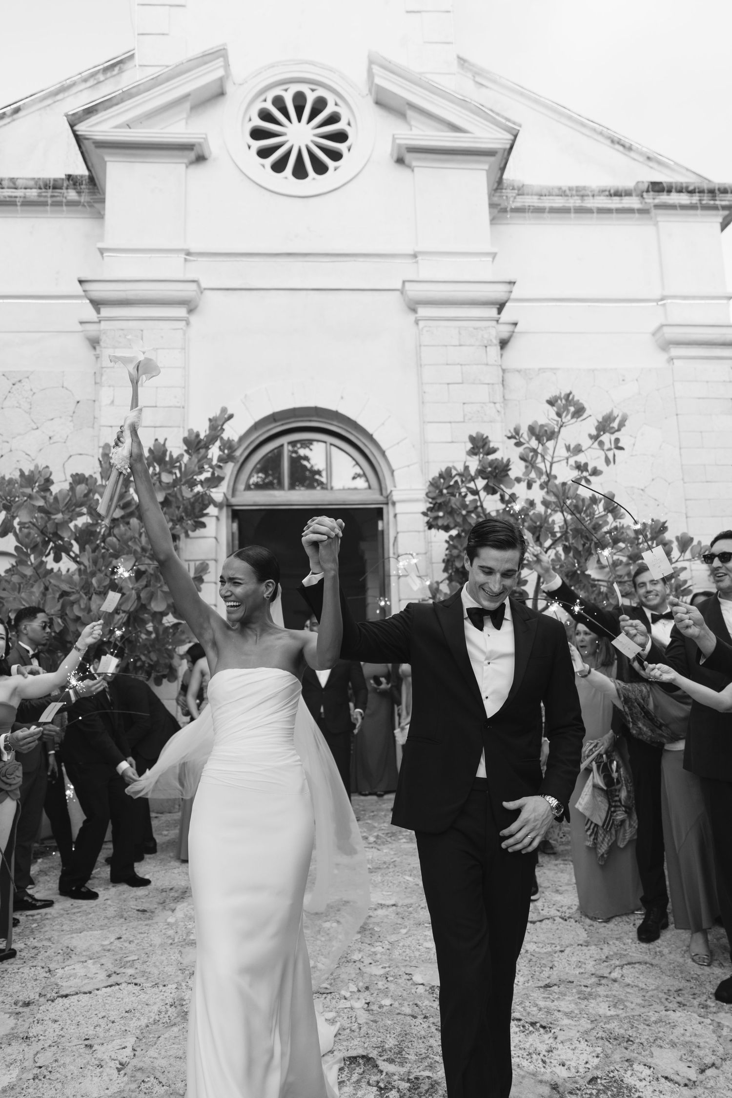 A black and white wedding photo showing a couple exiting a historic church building surrounded by guests.