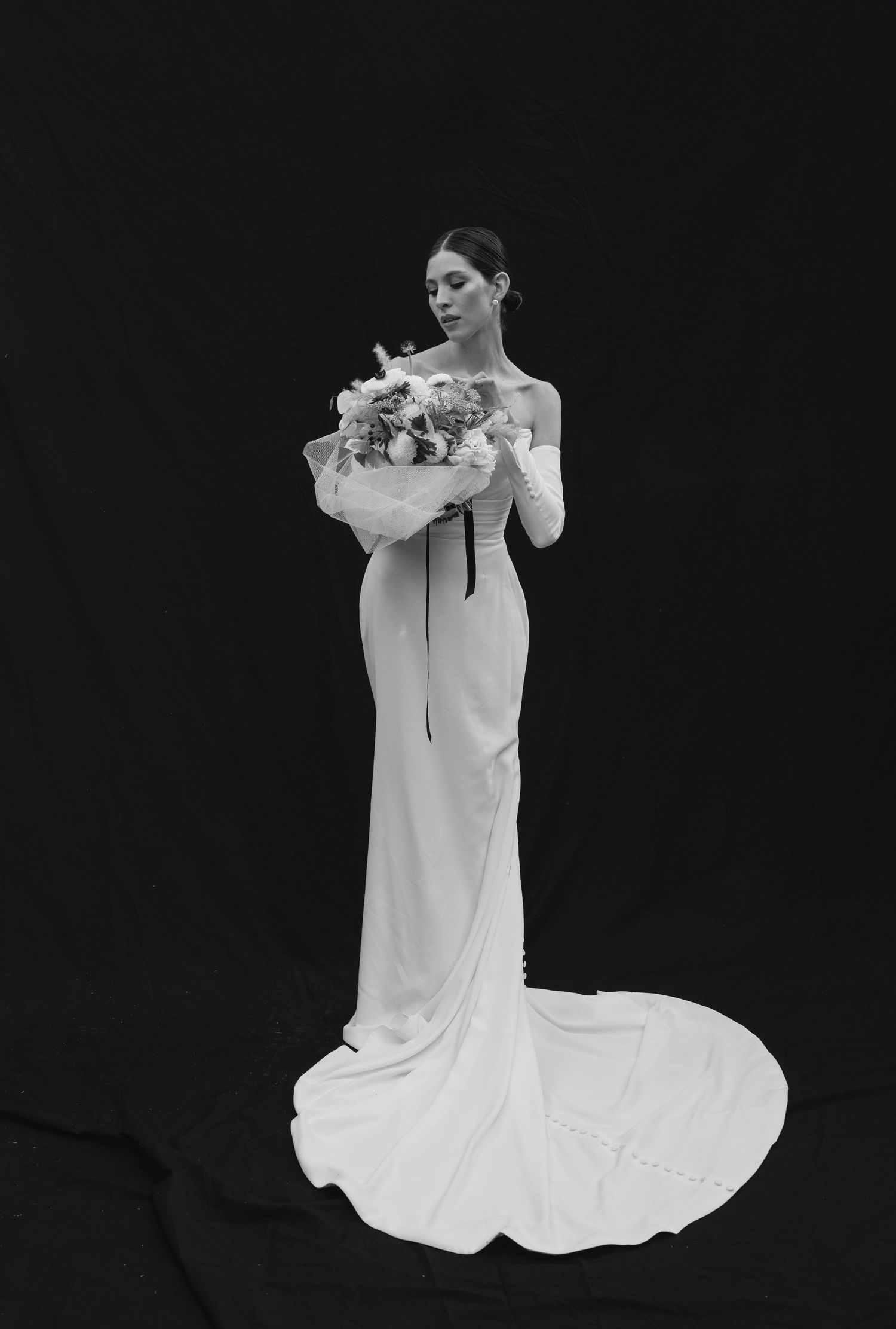 Elegant black and white bridal portrait featuring a sleek fitted dress with dramatic train and bouquet.