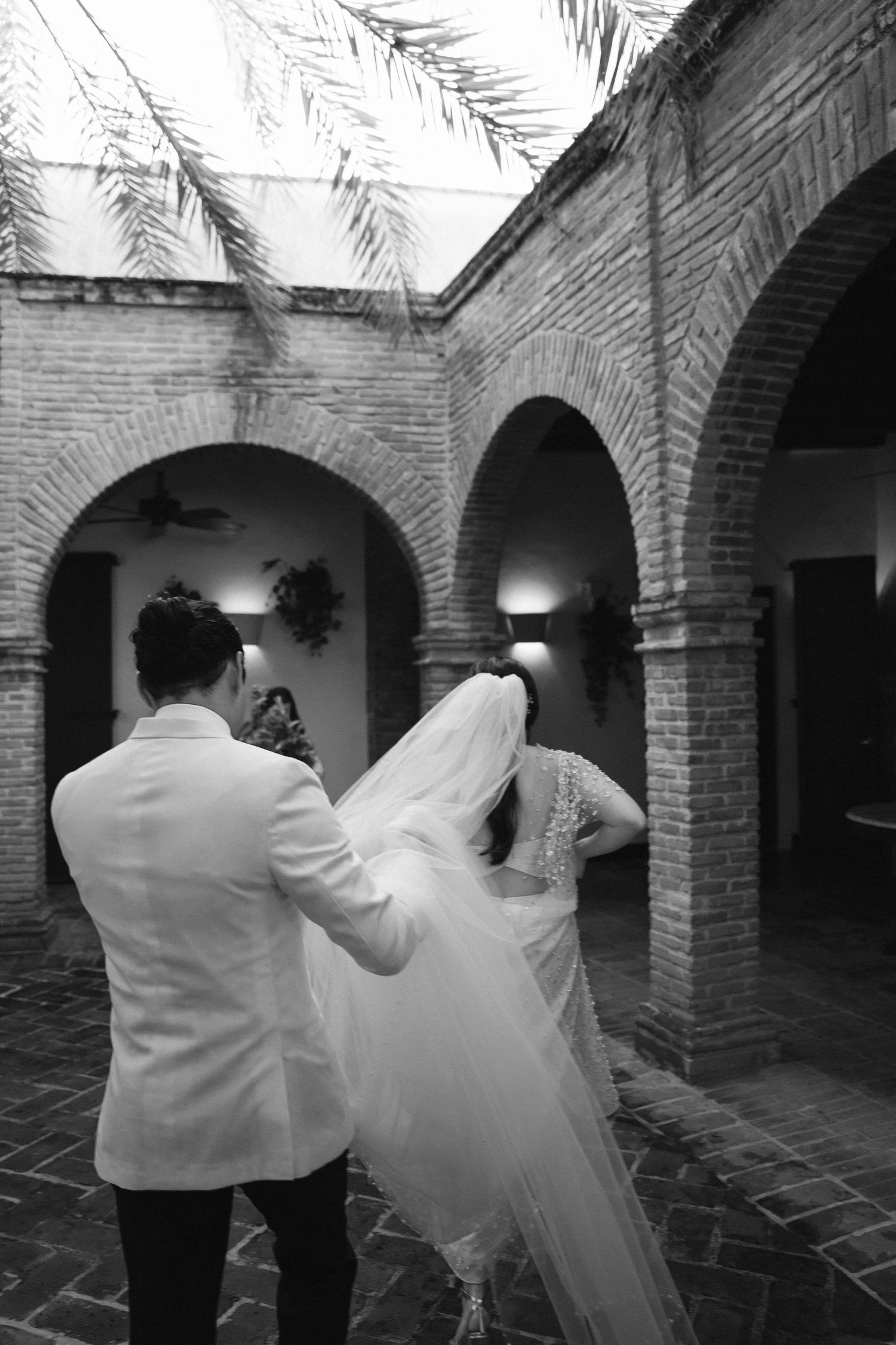 Black and white photo of couple dancing under brick archways at wedding venue.