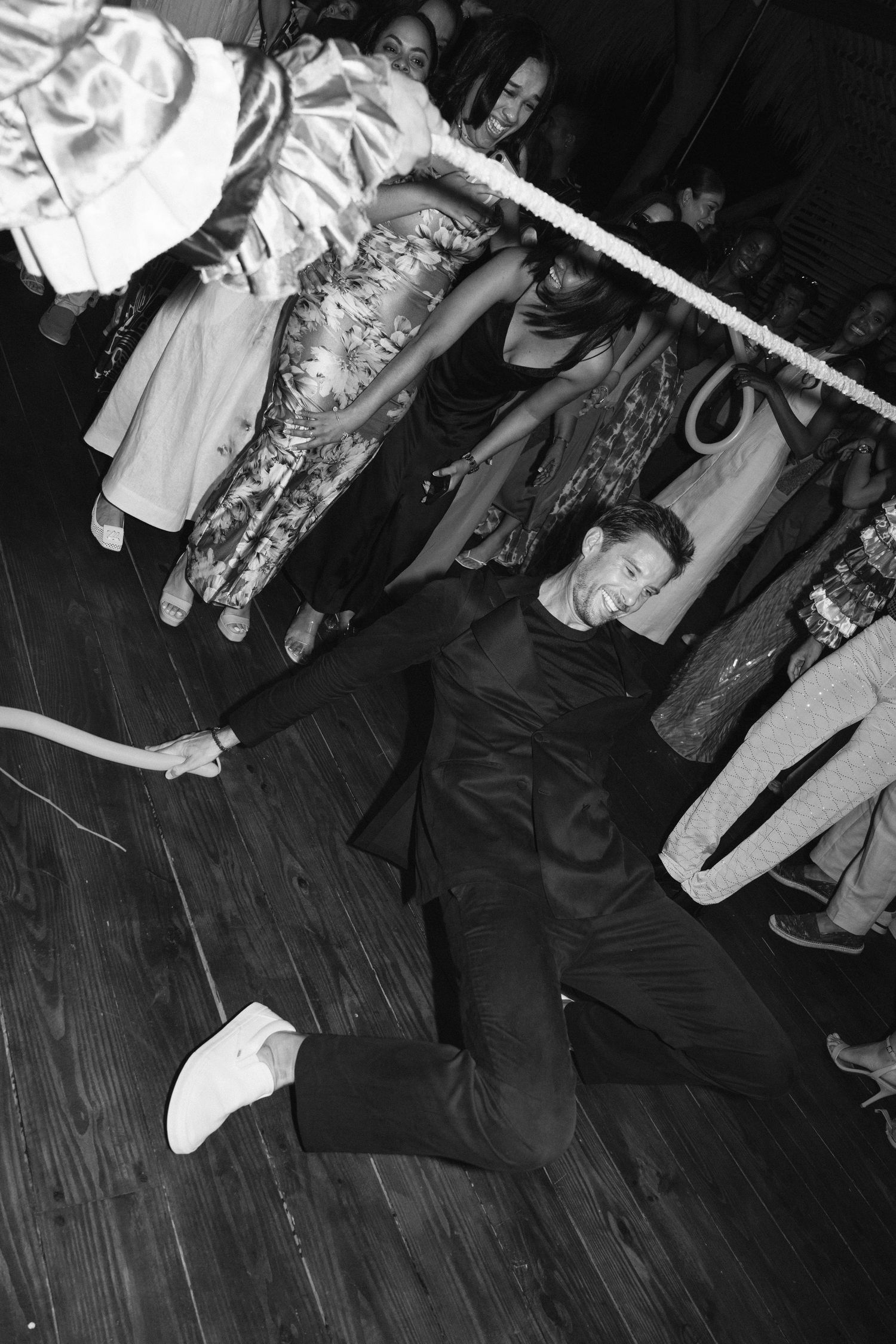 A person in dark clothing performs a limbo dance move under a bar at what appears to be a party on a wooden floor.