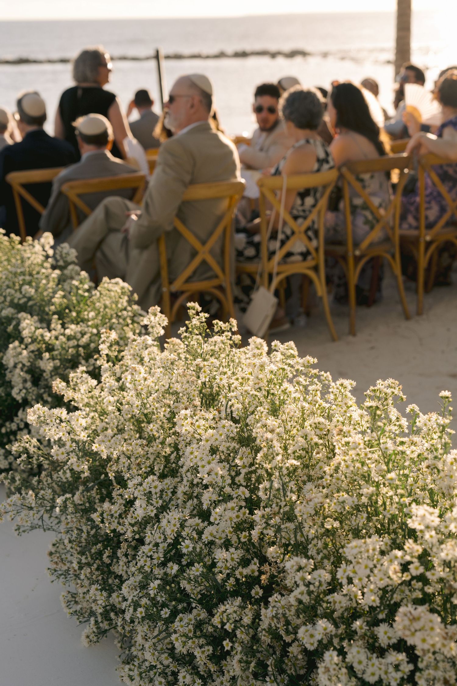 Wedding guests seated at outdoor reception with delicate white baby's breath floral arrangements in foreground.