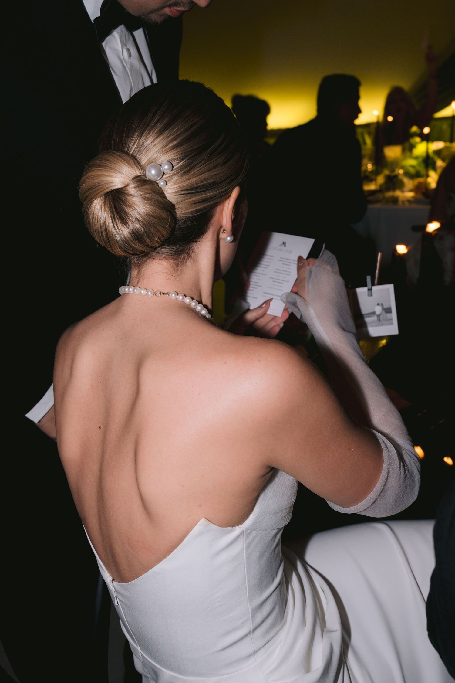 Bride in strapless gown writing in notebook at reception, elegant updo hairstyle visible.