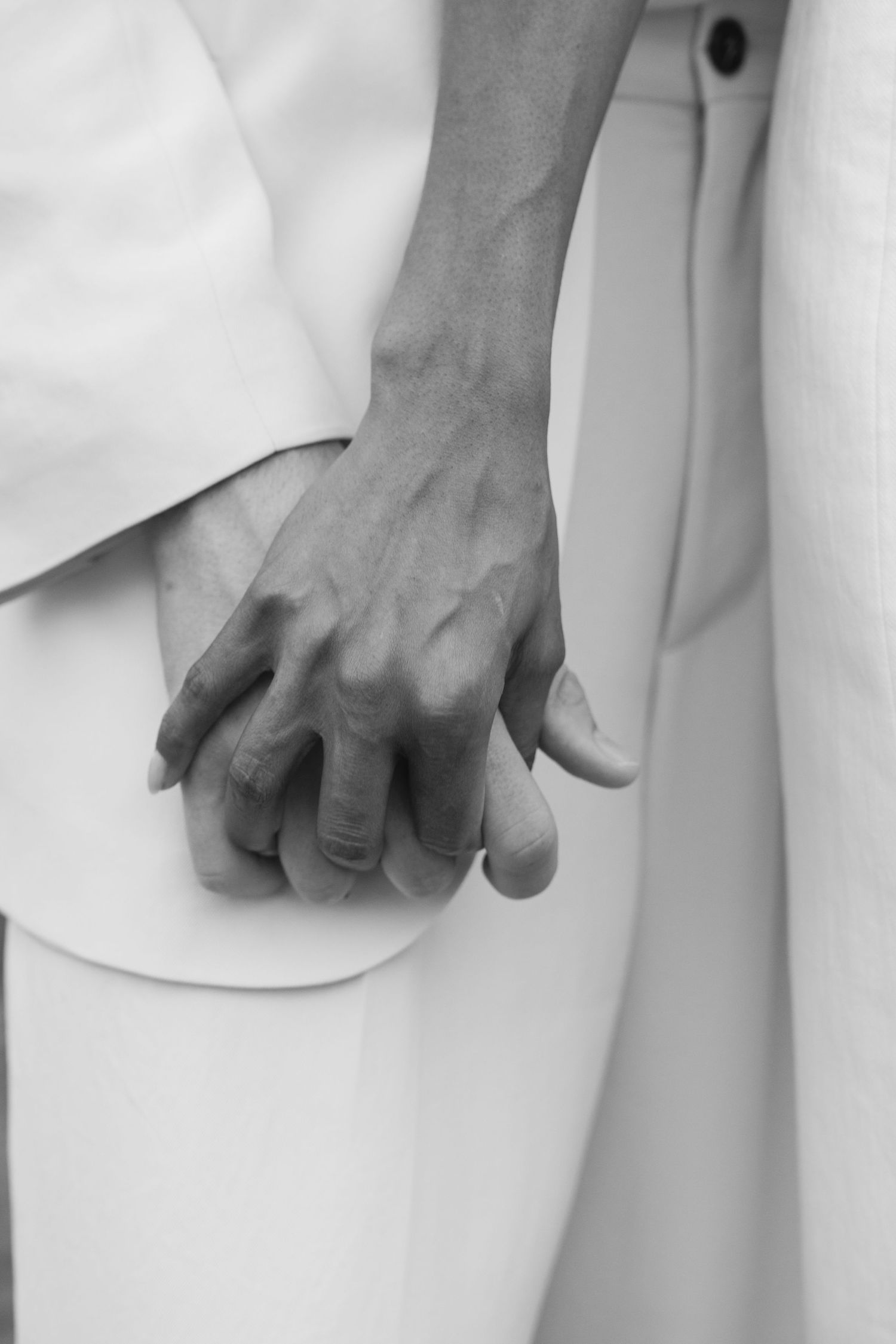 Black and white close-up image of a hand resting against white fabric, showing veins and natural skin texture.