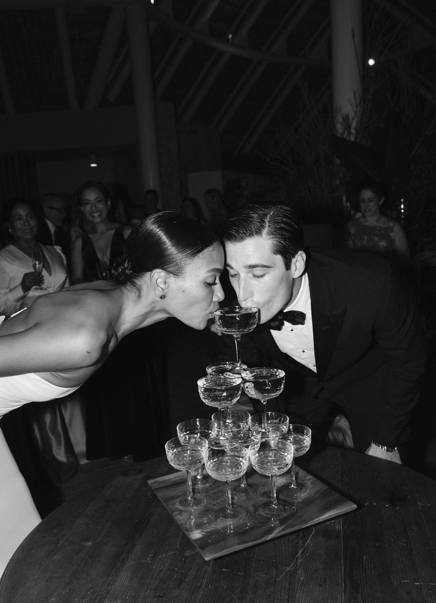 A vintage black and white photo showing a couple sipping from a champagne tower at a formal event.