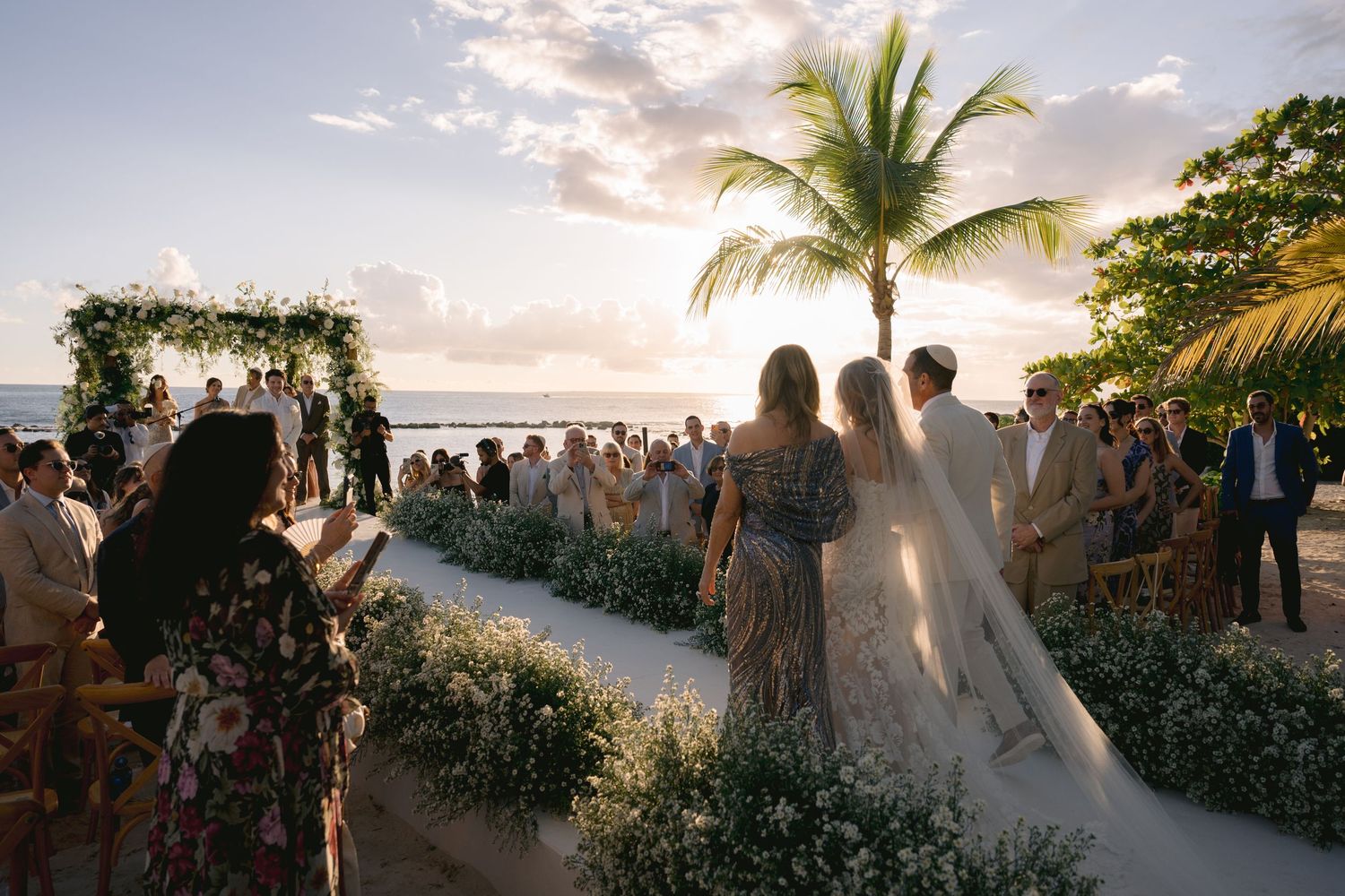A scenic beach wedding ceremony setup with palm trees and ocean views during golden hour sunset.