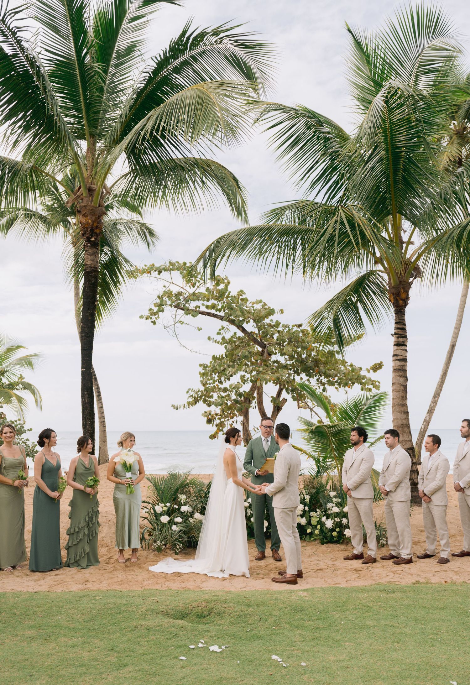 A beach wedding ceremony with wedding party lined up under palm trees.
