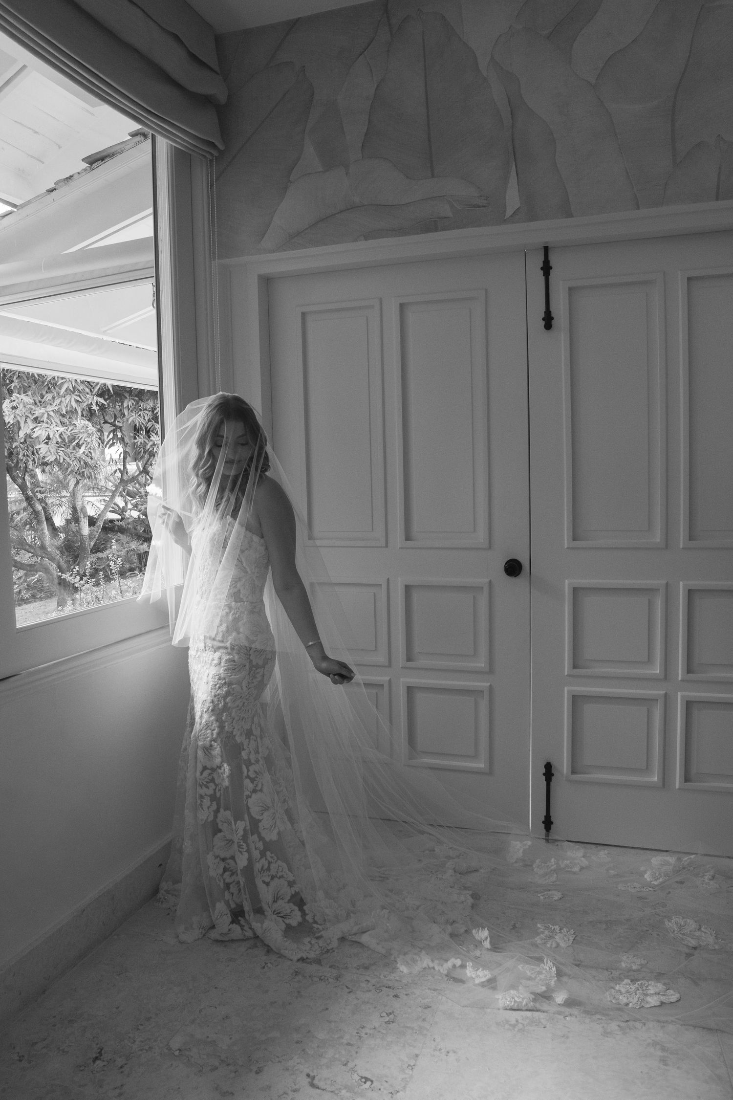 A figure in a flowing white dress and veil moves mysteriously through an empty white room in a series of haunting poses.