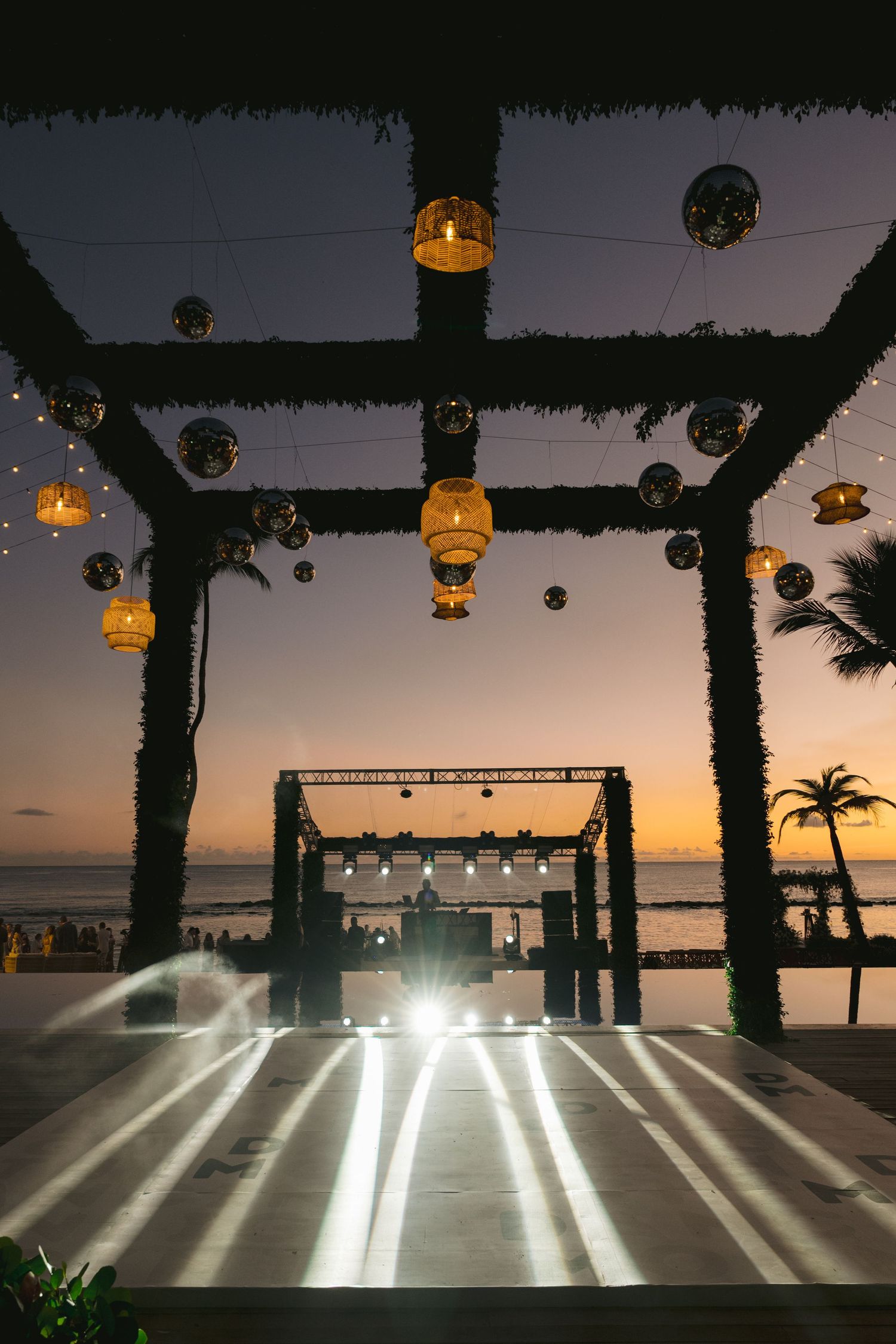 Sunset view of an empty beach club dance floor with illuminated stripes and hanging disco balls at dusk.