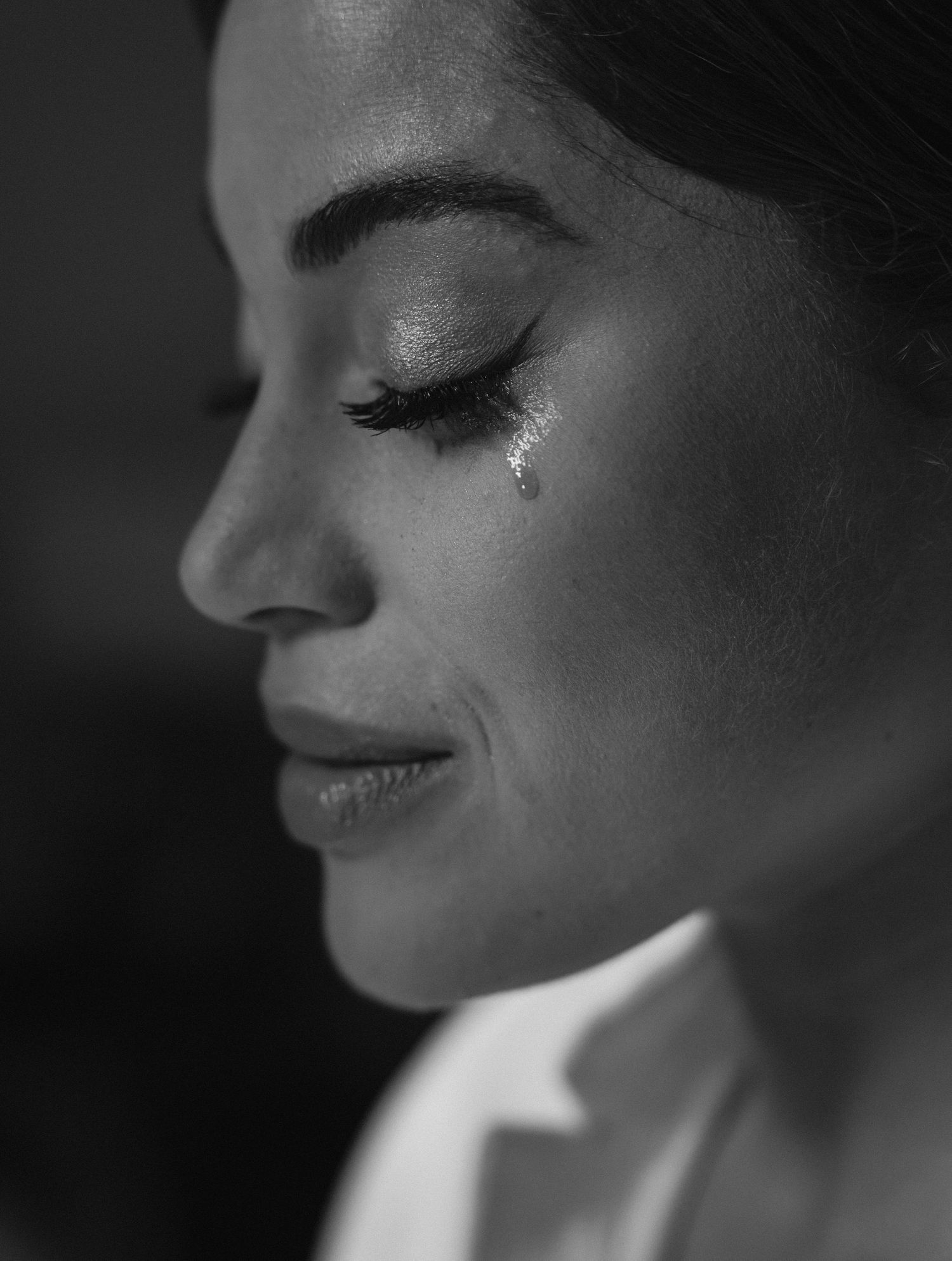 Dramatic black and white close-up portrait showing glitter tear detail and serene expression.