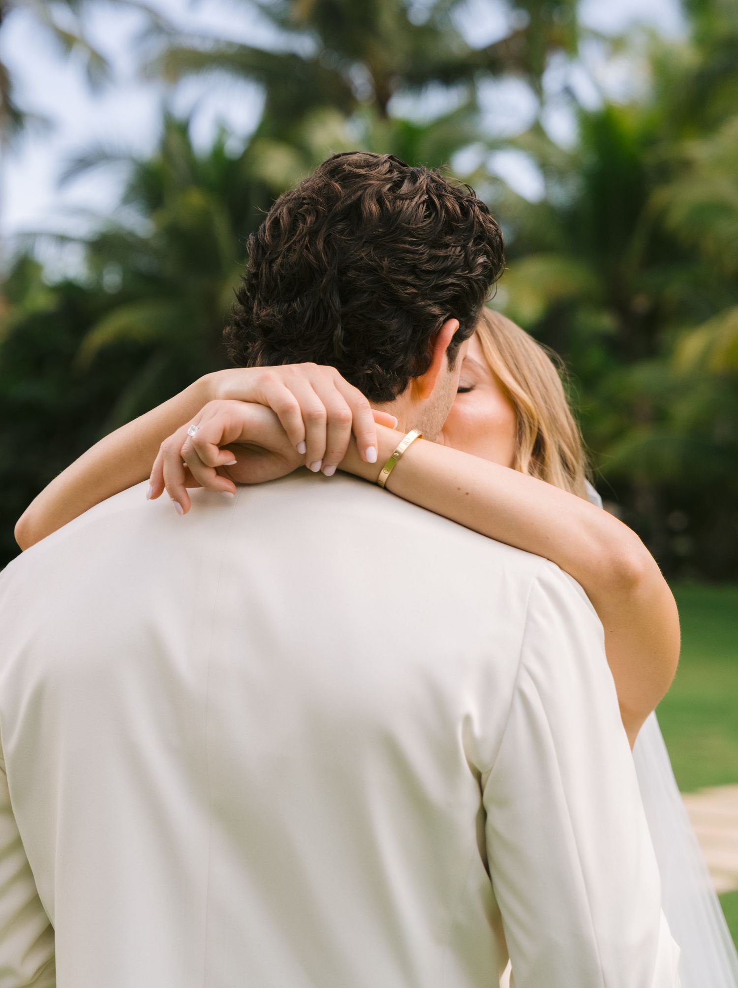 A couple in white clothing sharing an intimate kiss in a lush outdoor garden setting.