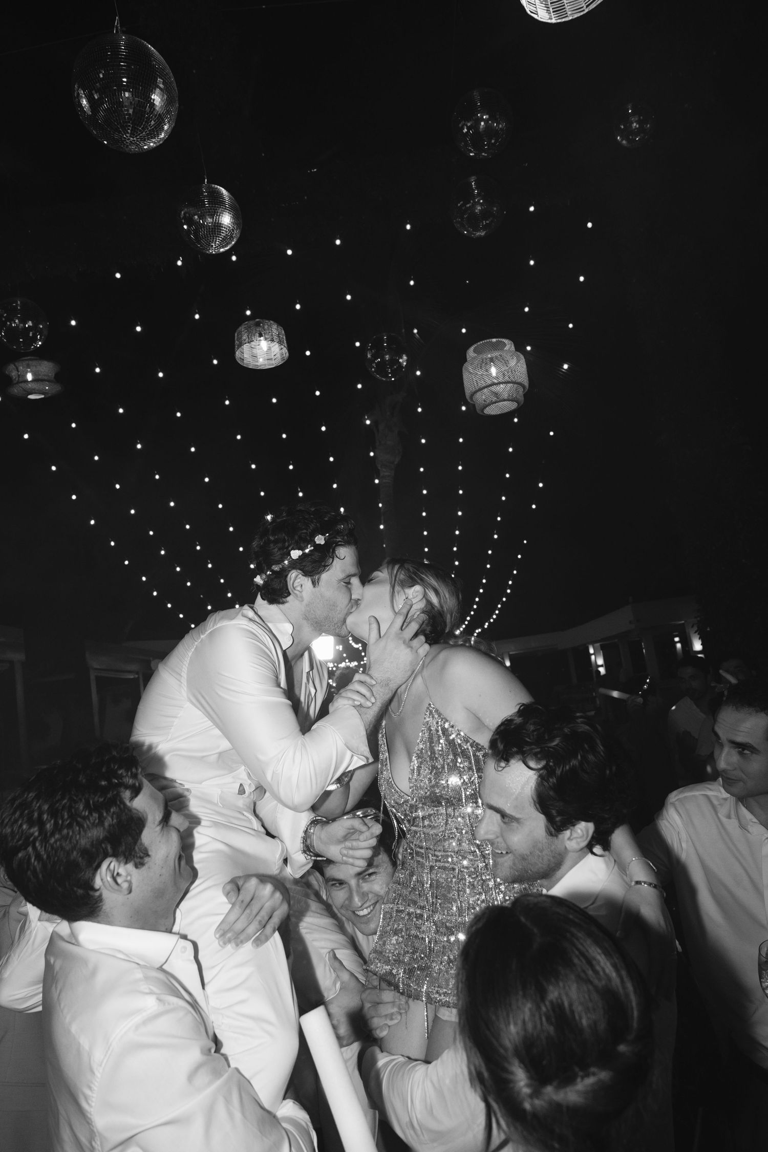 A couple shares a romantic moment on a dance floor under glittering disco balls and string lights at a nightclub.
