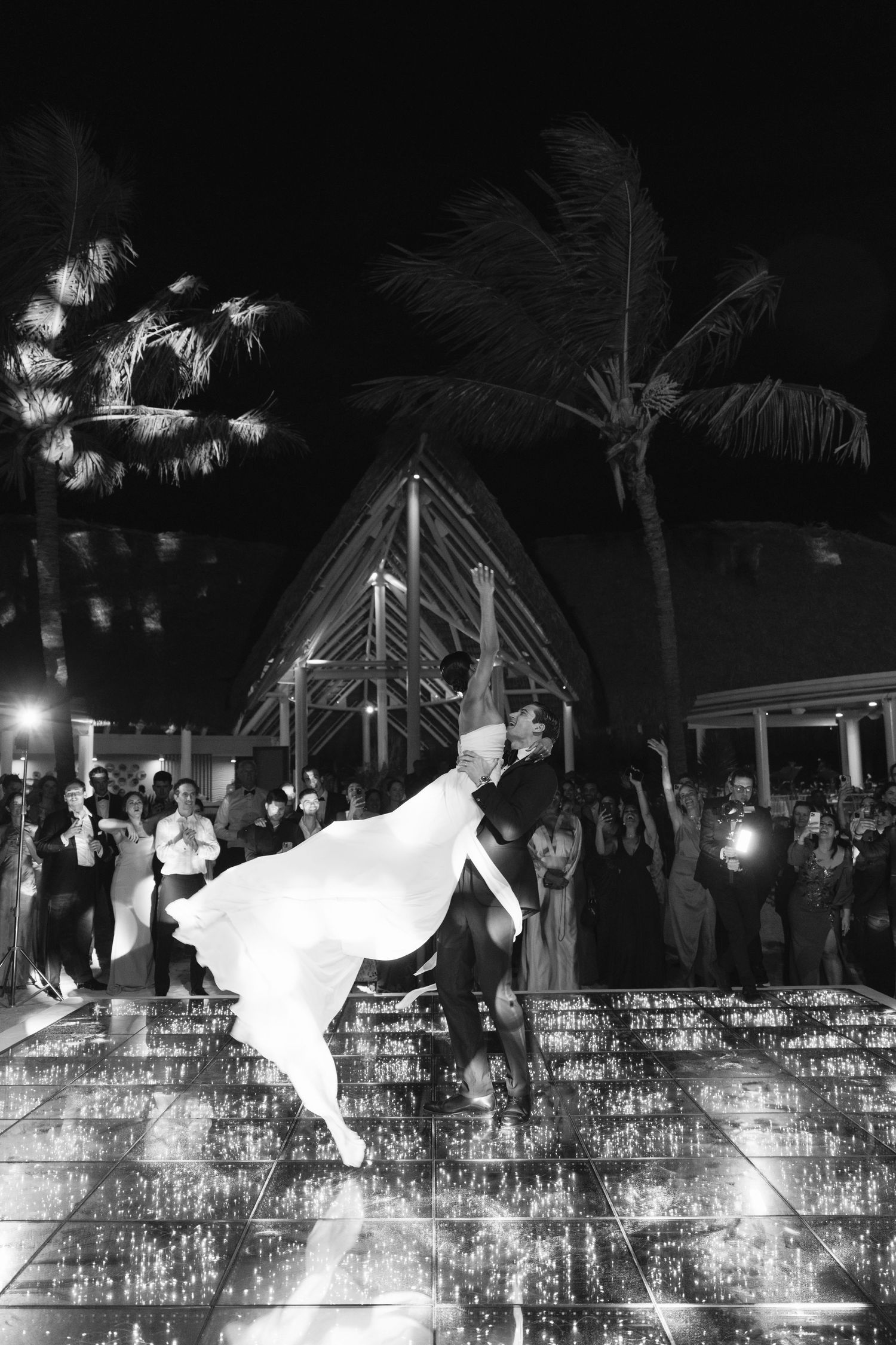 Romantic dance on a reflective surface at night with palm trees and party lights creating a magical atmosphere.