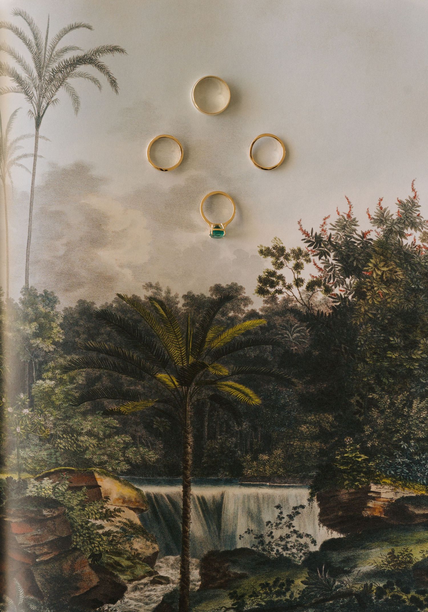 Wedding rings arranged on a vintage tropical landscape artwork featuring palm trees and a waterfall.