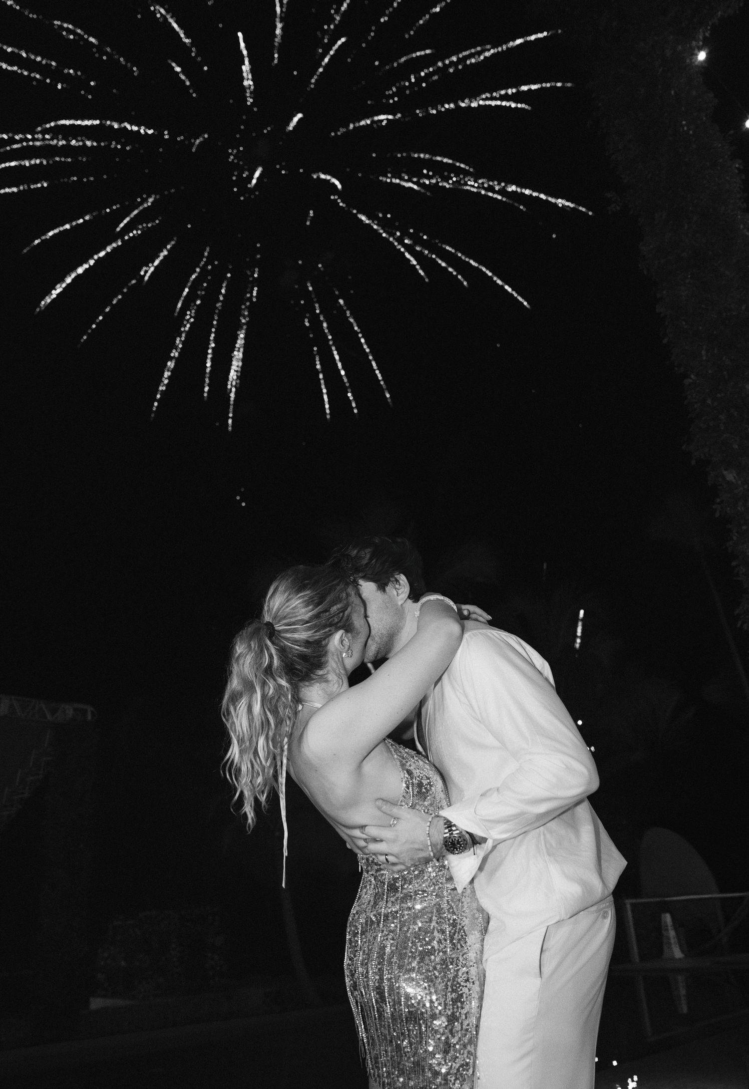 Couple sharing a romantic kiss under bursting fireworks in the night sky during a celebration.