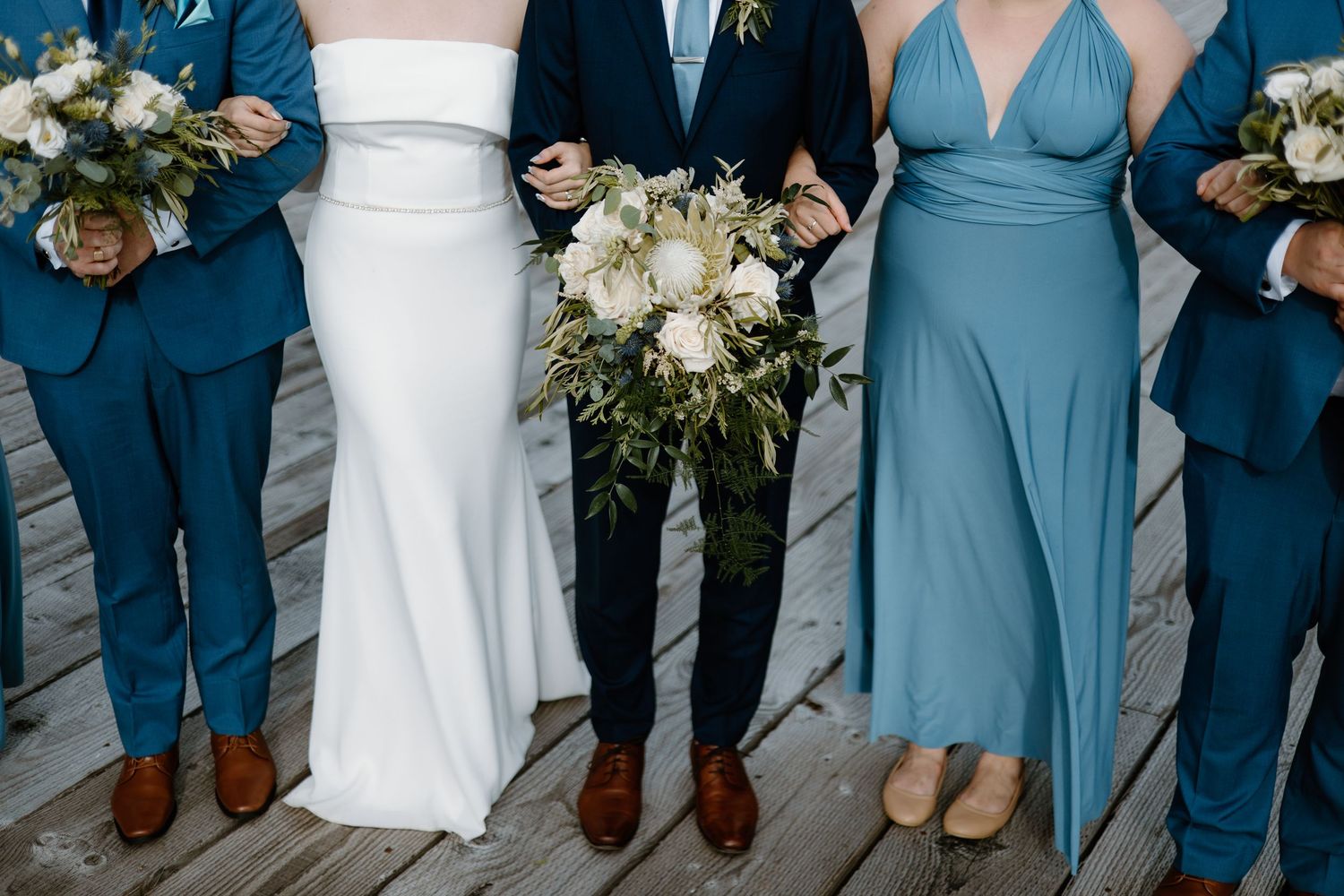 Detail shot of wedding party attire showing navy suits and dusty blue dresses with bouquets.