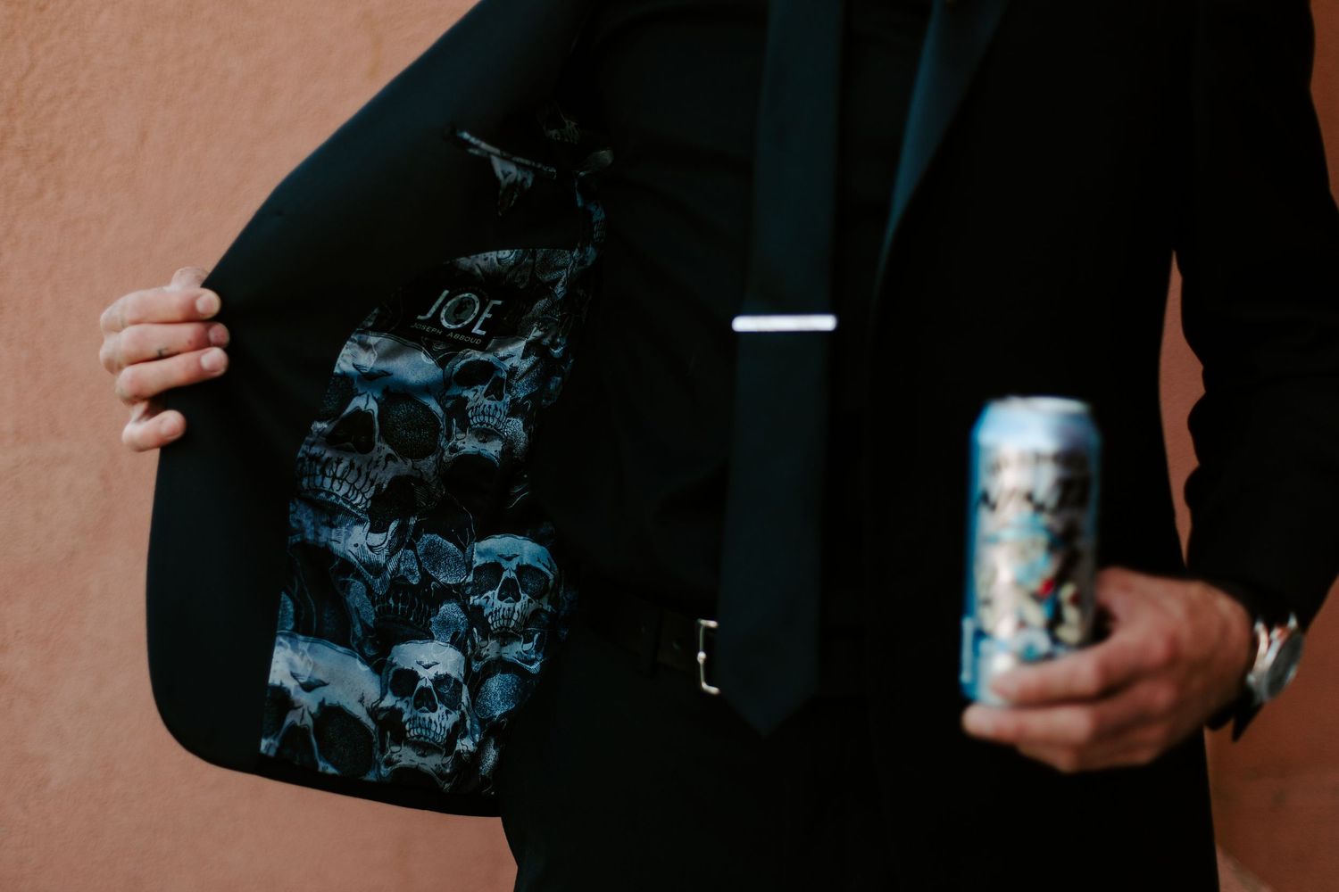 A person in black clothing holds a can of Pabst Blue Ribbon beer against a dark background.