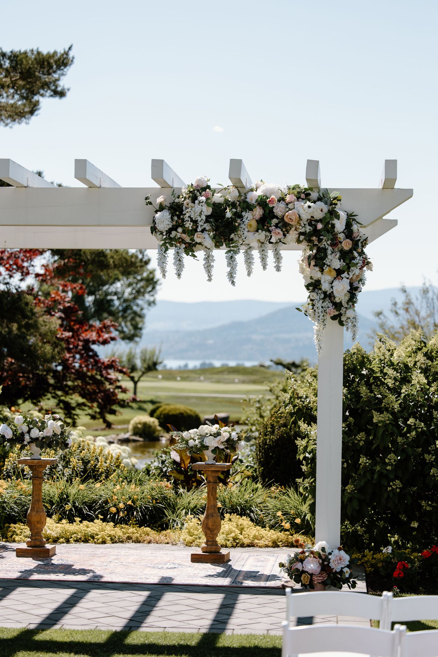White wedding pergola decorated with lush floral arrangements overlooking mountain landscape.