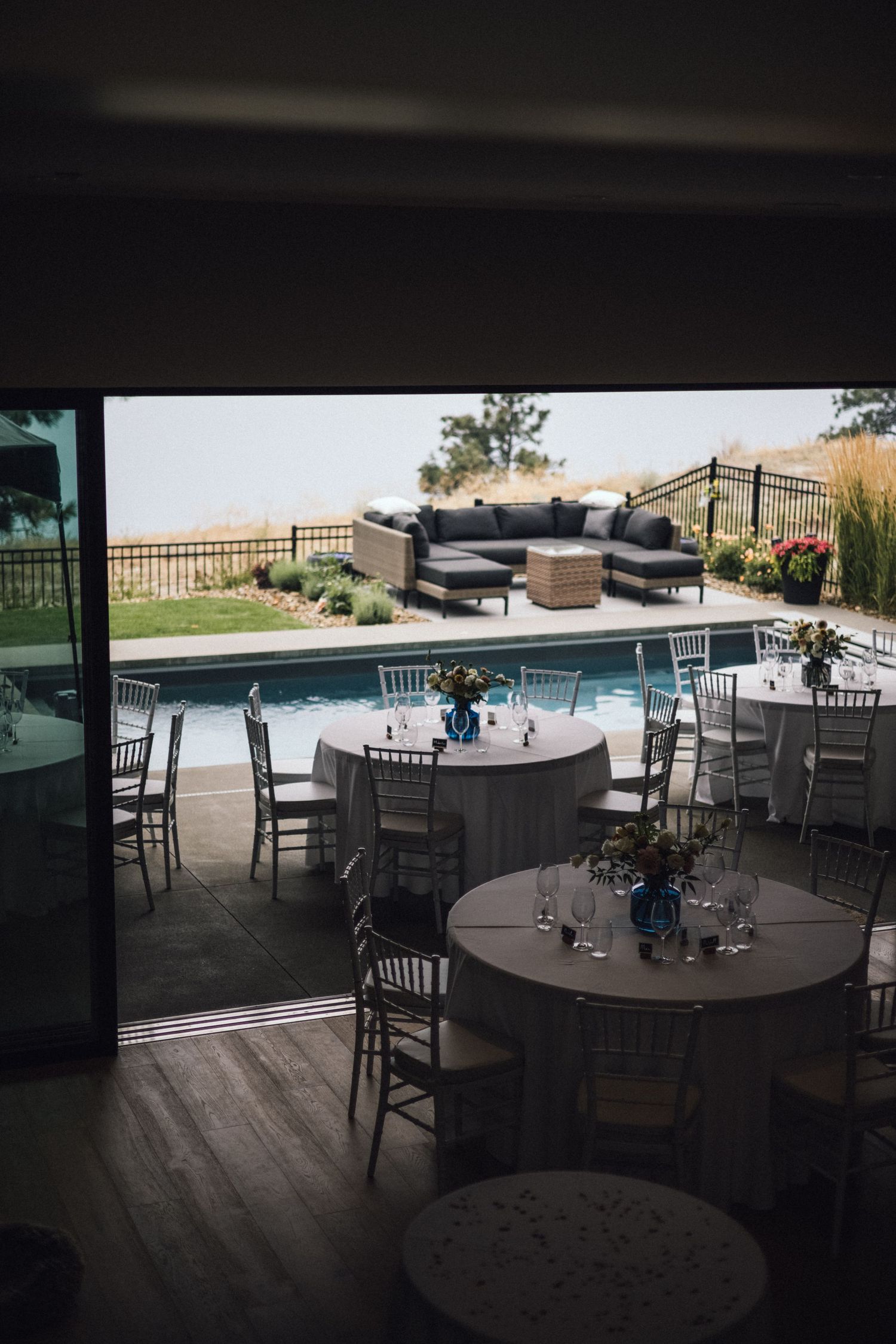 An outdoor wedding reception setup with tables and chairs arranged around a swimming pool with mountain views.