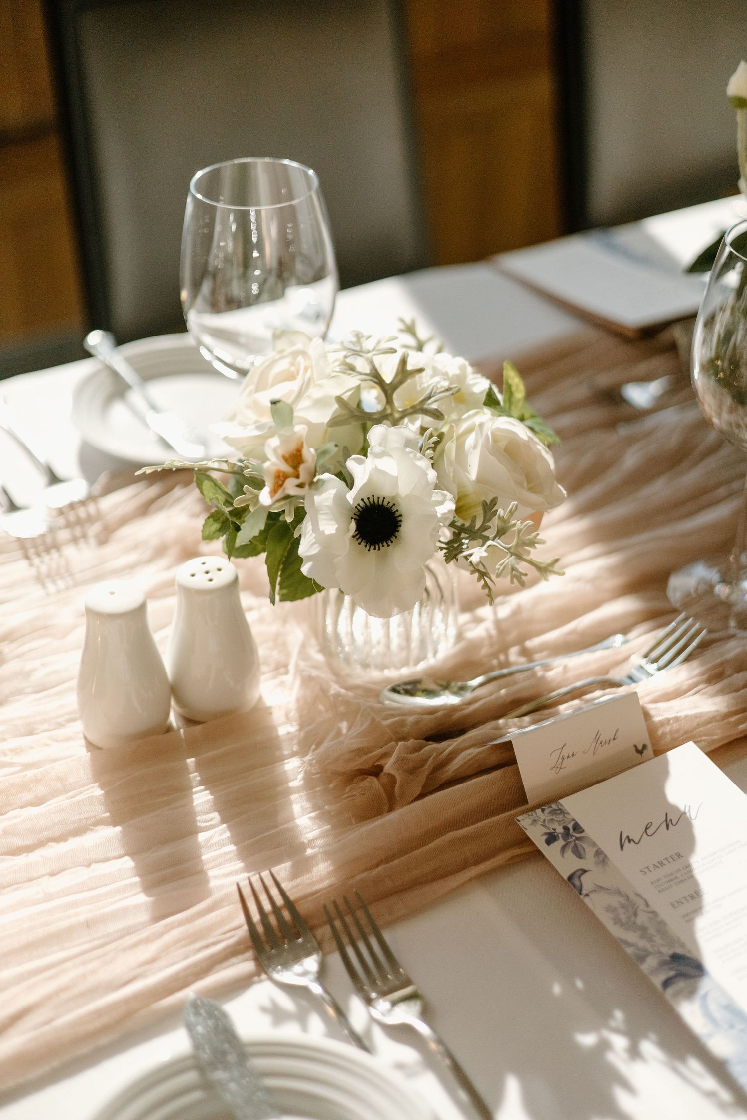 Intimate table setting with white anemone centerpiece and golden sunlight streaming across.