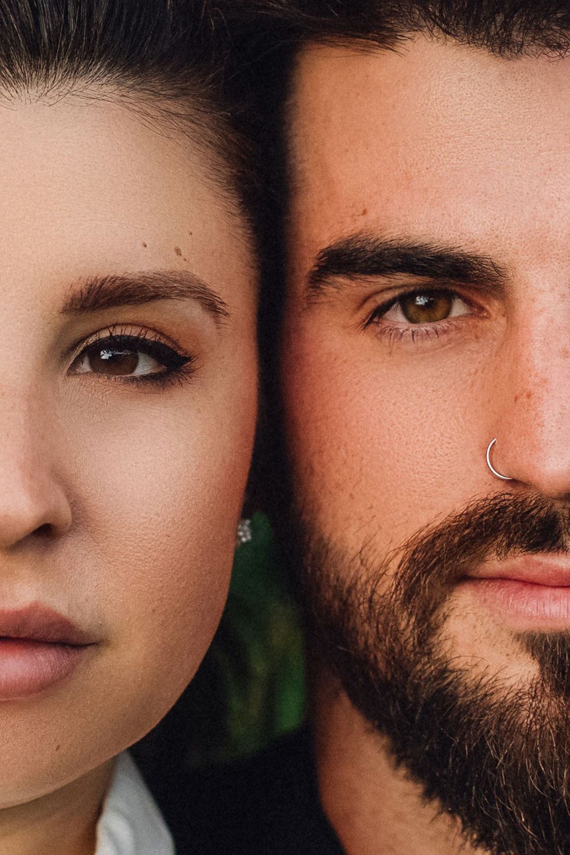 Close-up portrait of a young couple side by side, woman with earring and man with nose ring and beard.