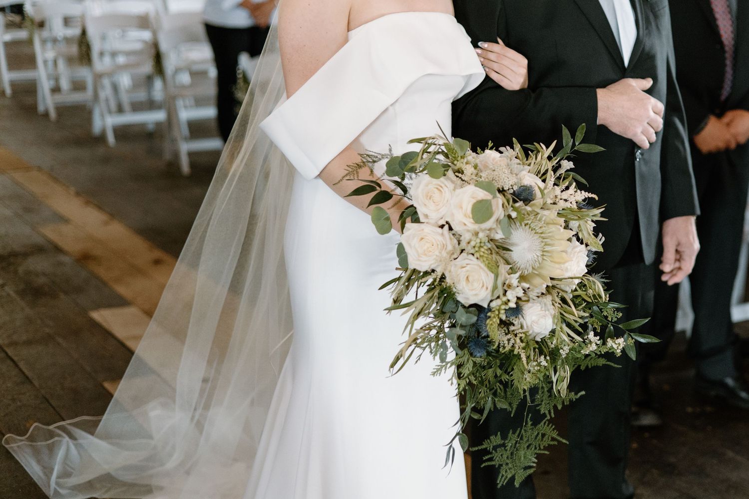 Elegant white bridal bouquet with cascading greenery against wedding dress.