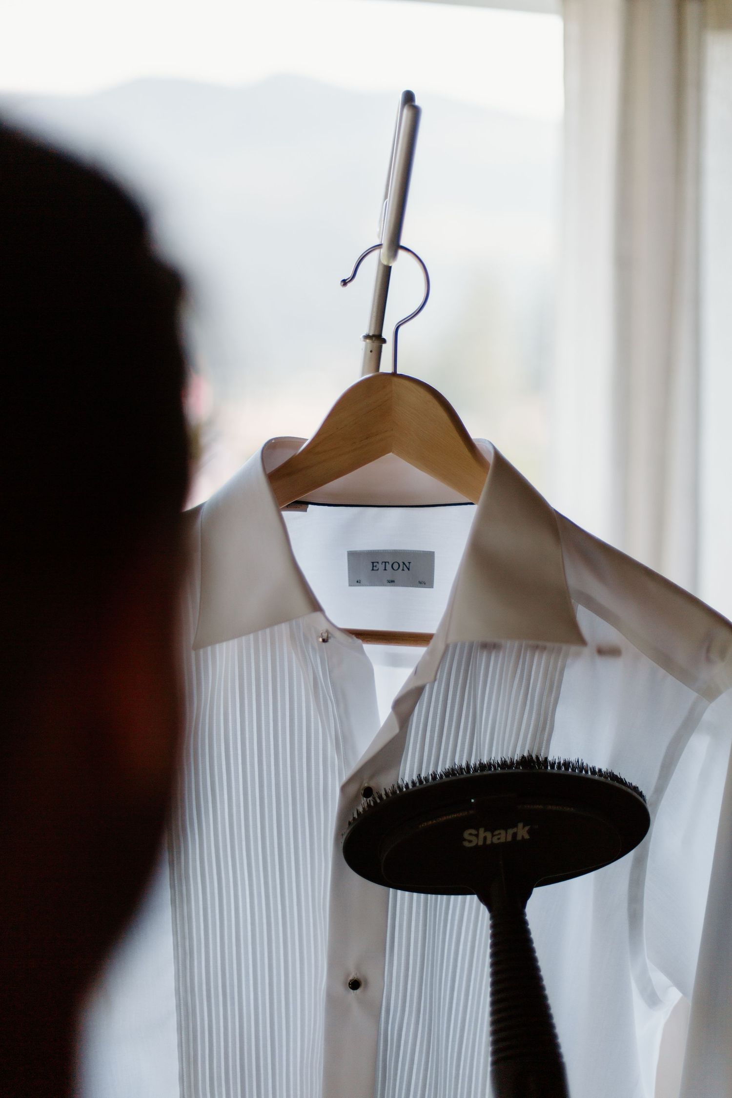 Close-up view of white dress shirts with pleated fronts hanging on wooden hangers.